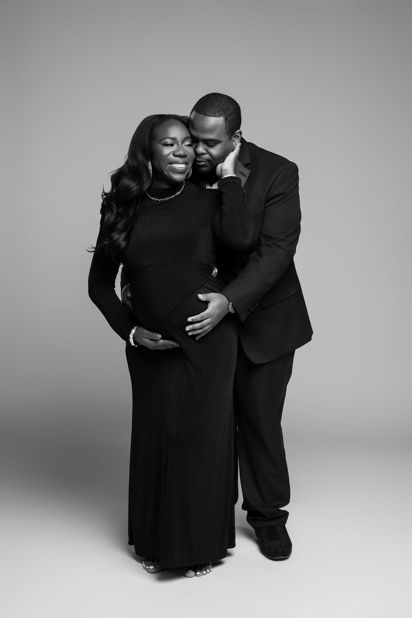 Intimate black and white portrait series showing a couple in matching black outfits embracing against a studio backdrop.