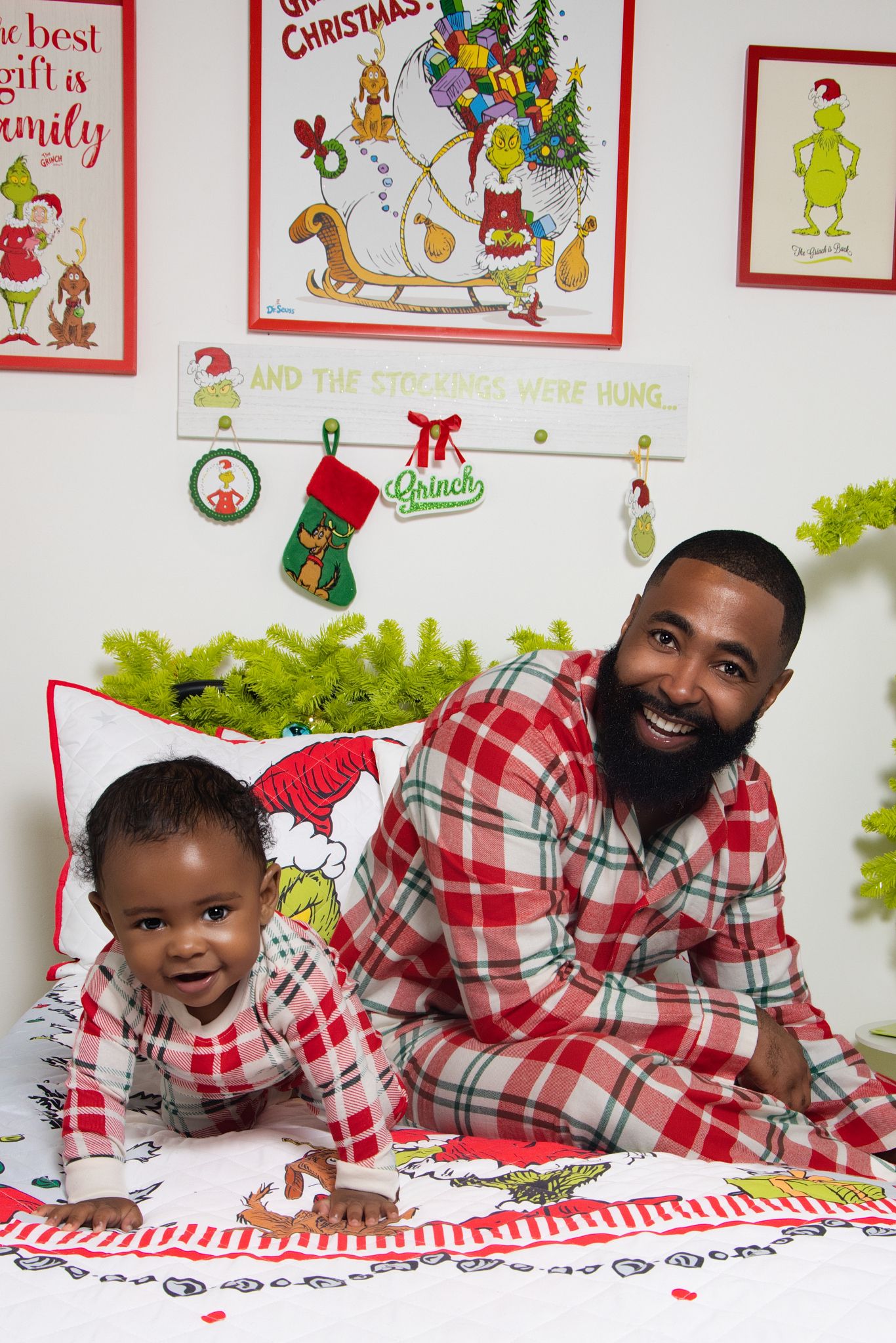 A family wearing matching red and white plaid pajamas lies together on a white floor with Christmas decorations.