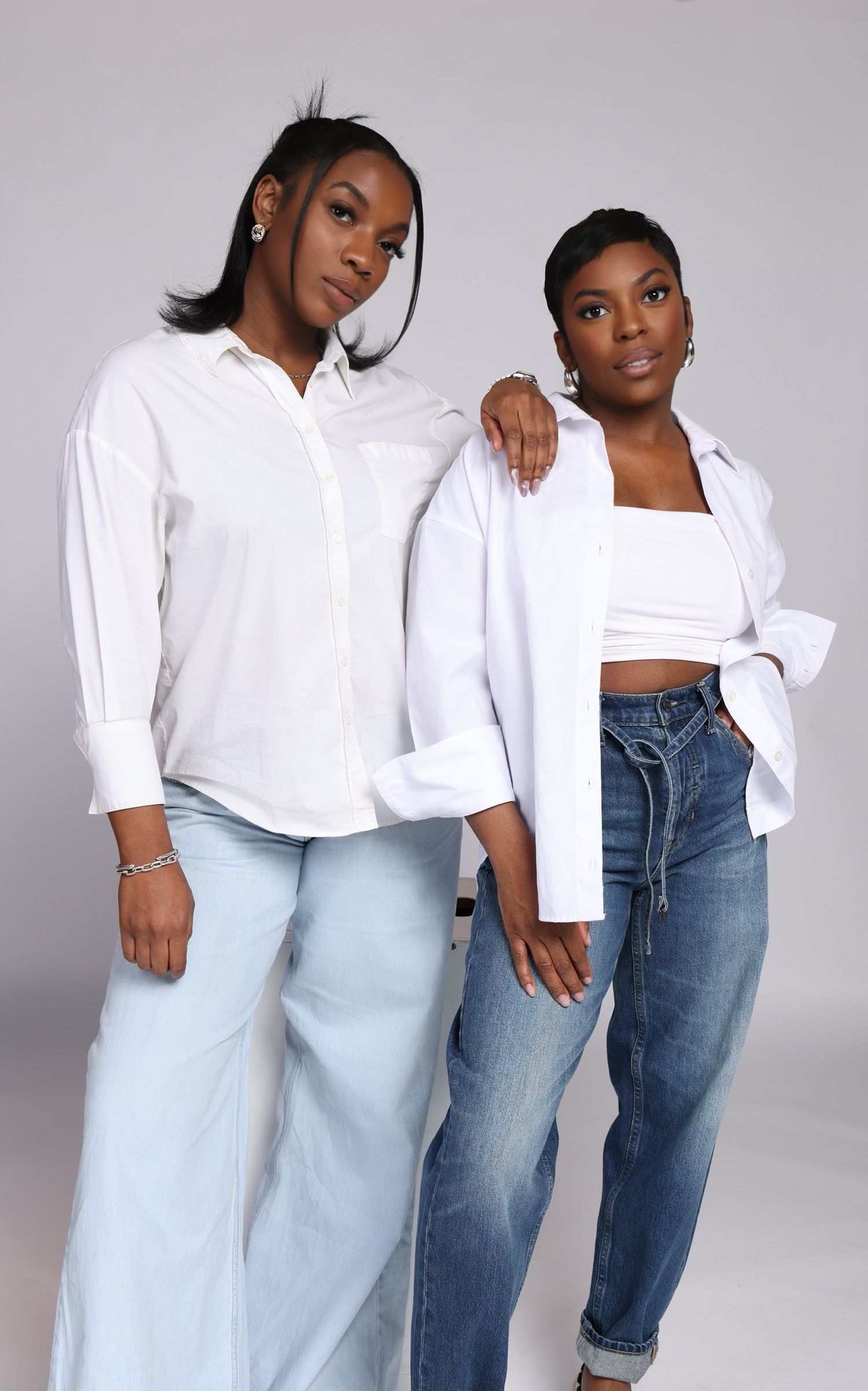 Two people wearing white shirts and jeans pose together in a professional studio setting.