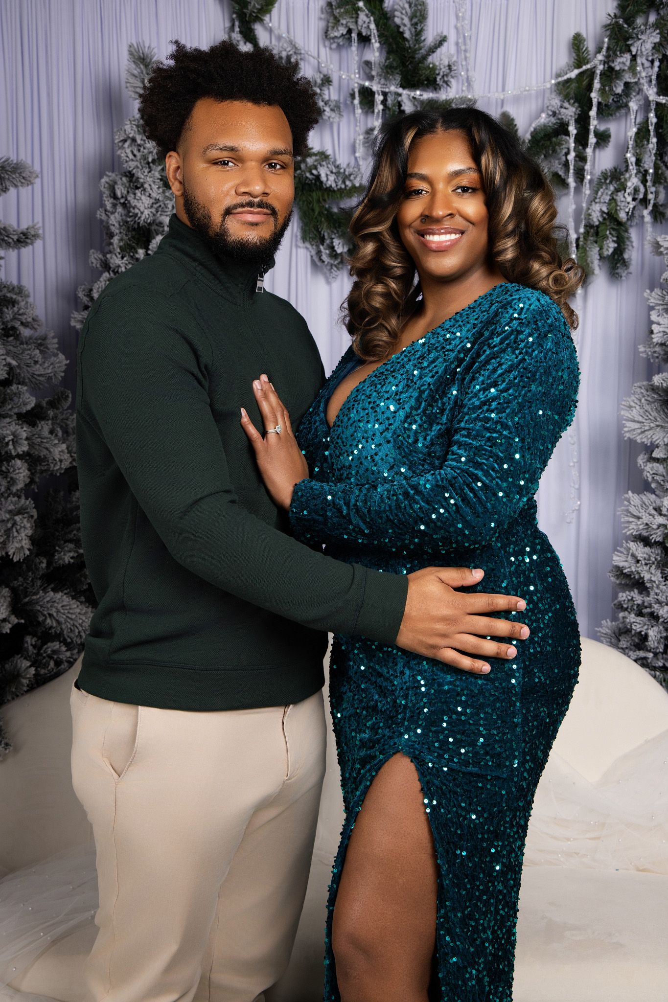 A couple poses together in a winter wonderland setting with a sparkling teal gown and dark green suit.