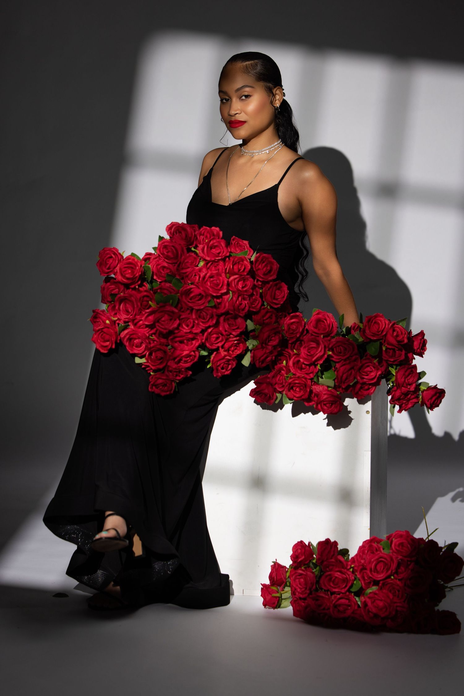 Stunning fashion photo featuring a black evening gown and dramatic red roses creating contrast against shadowy lighting.