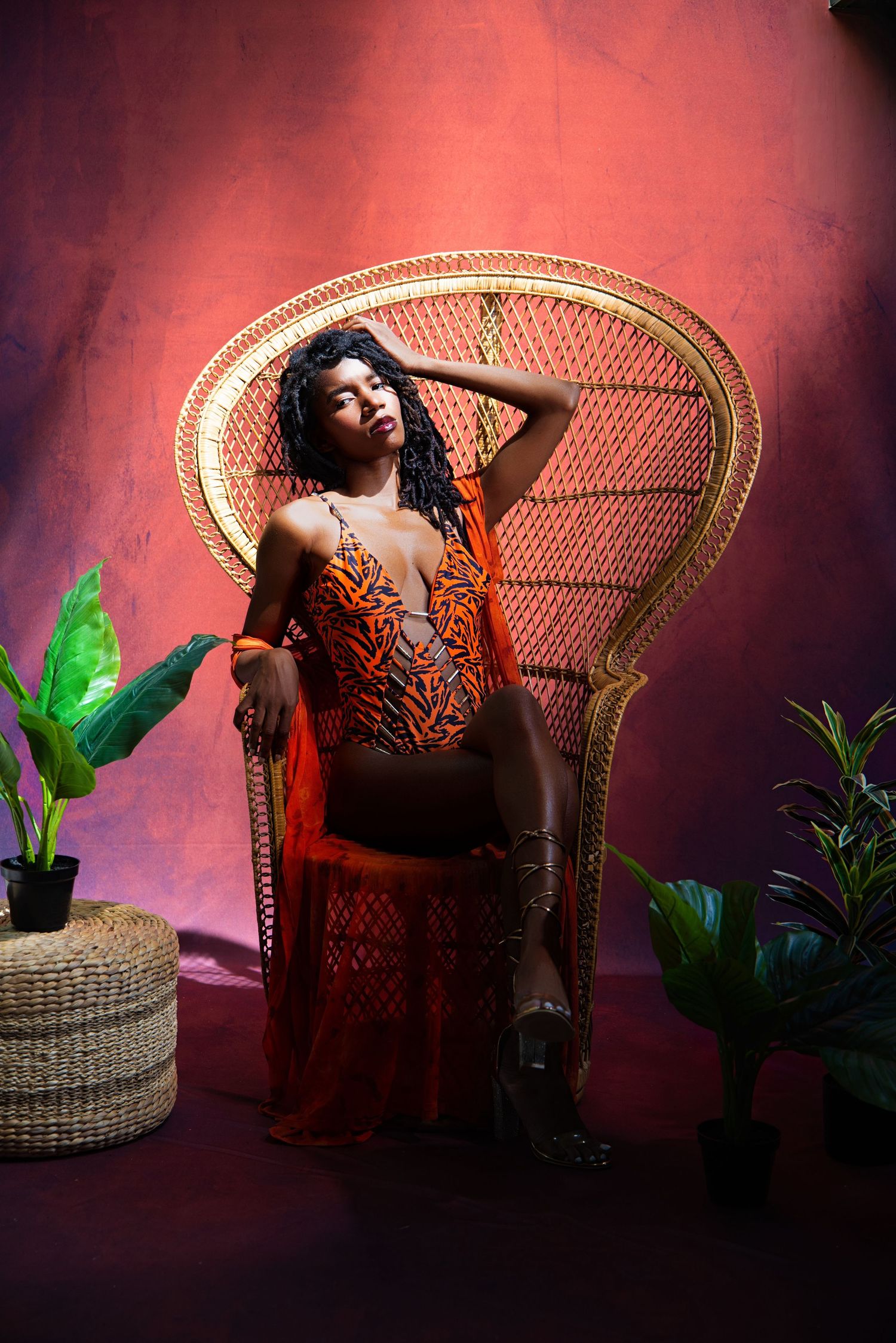 Artistic portrait with model lounging in wicker chair against red background.