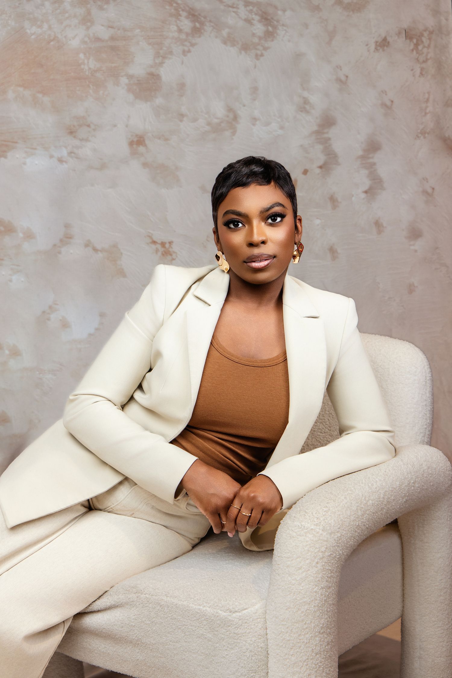 Professional studio portraits featuring a stylish white suit and brown top against a textured beige backdrop.