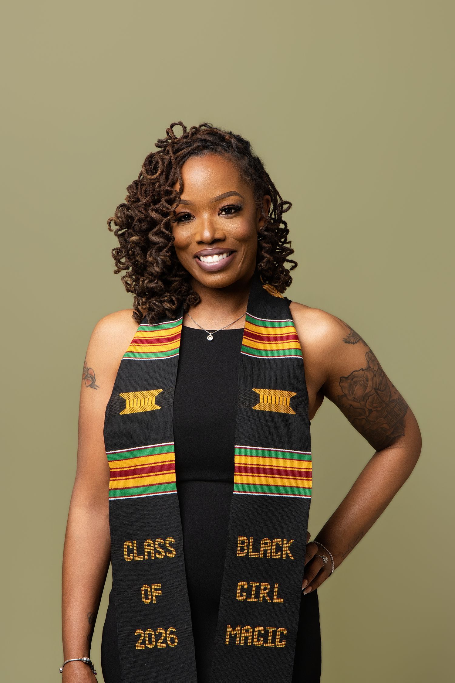 Woman wearing Kente cloth graduation stole reading Class of 2026 and Black Girl Magic, smiling confidently.