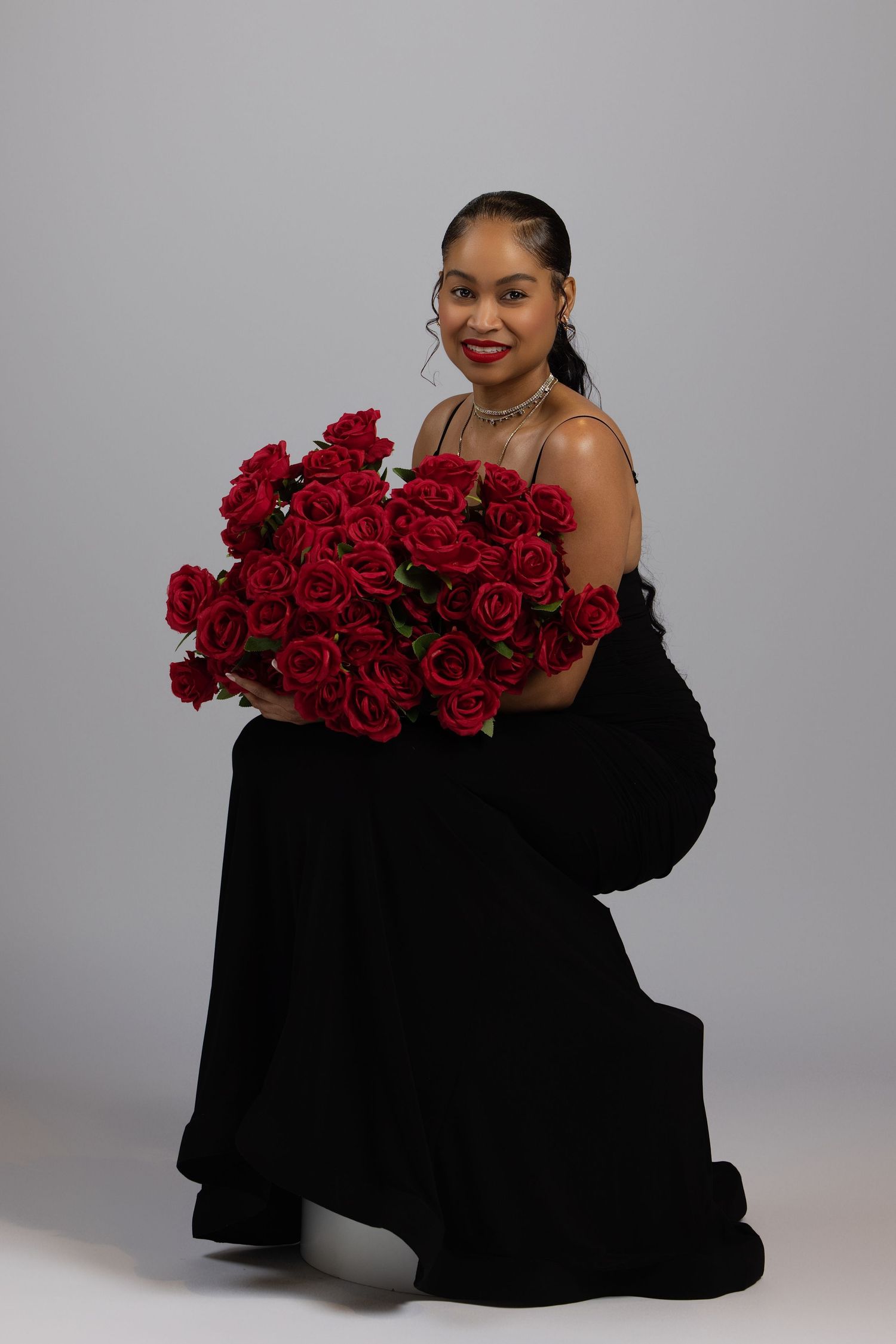 A figure in a black dress poses on the floor with vibrant red roses in an artistic photoshoot setup.