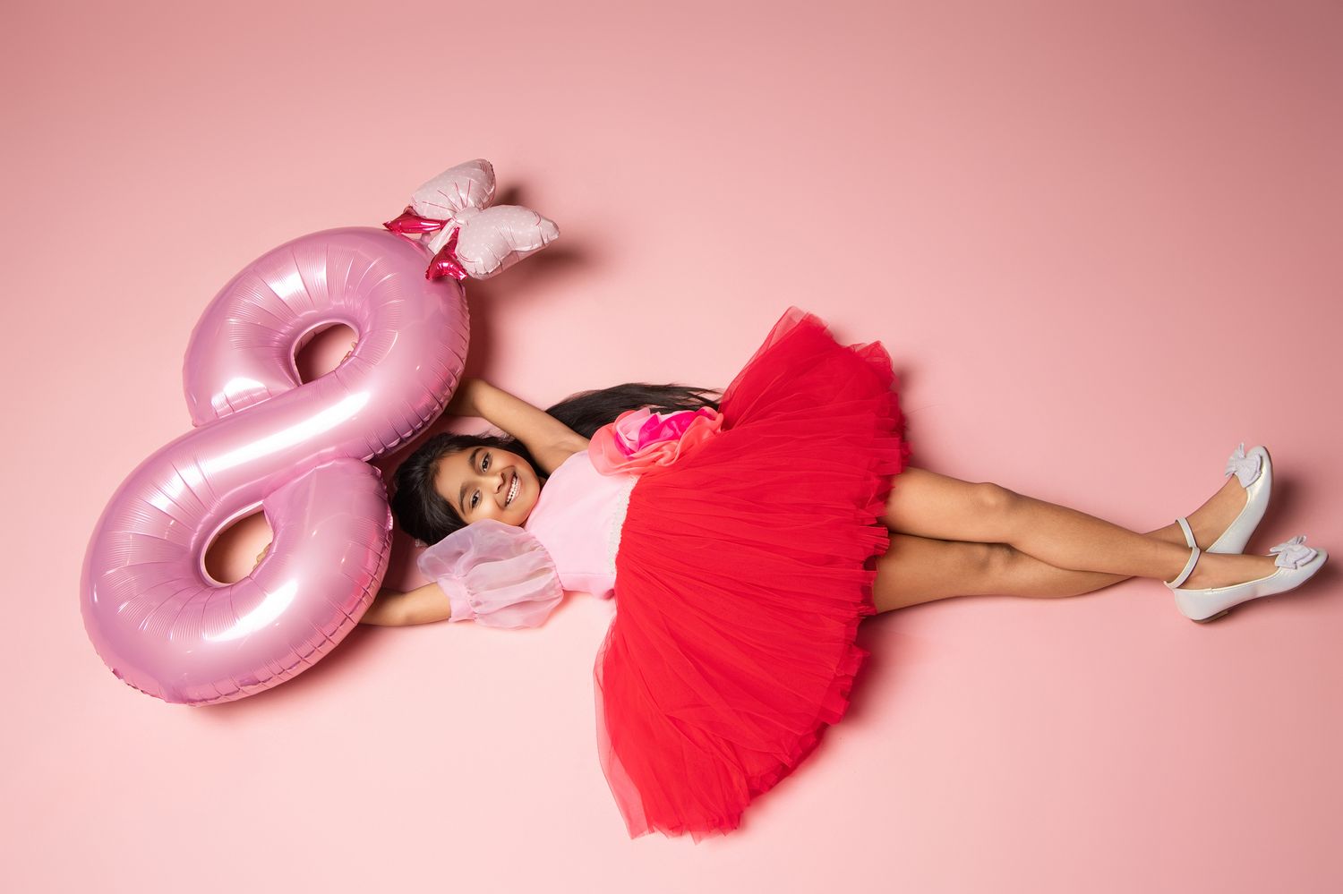 Pink glazed donut and red tulle fabric create an artistic composition on a soft pink background.