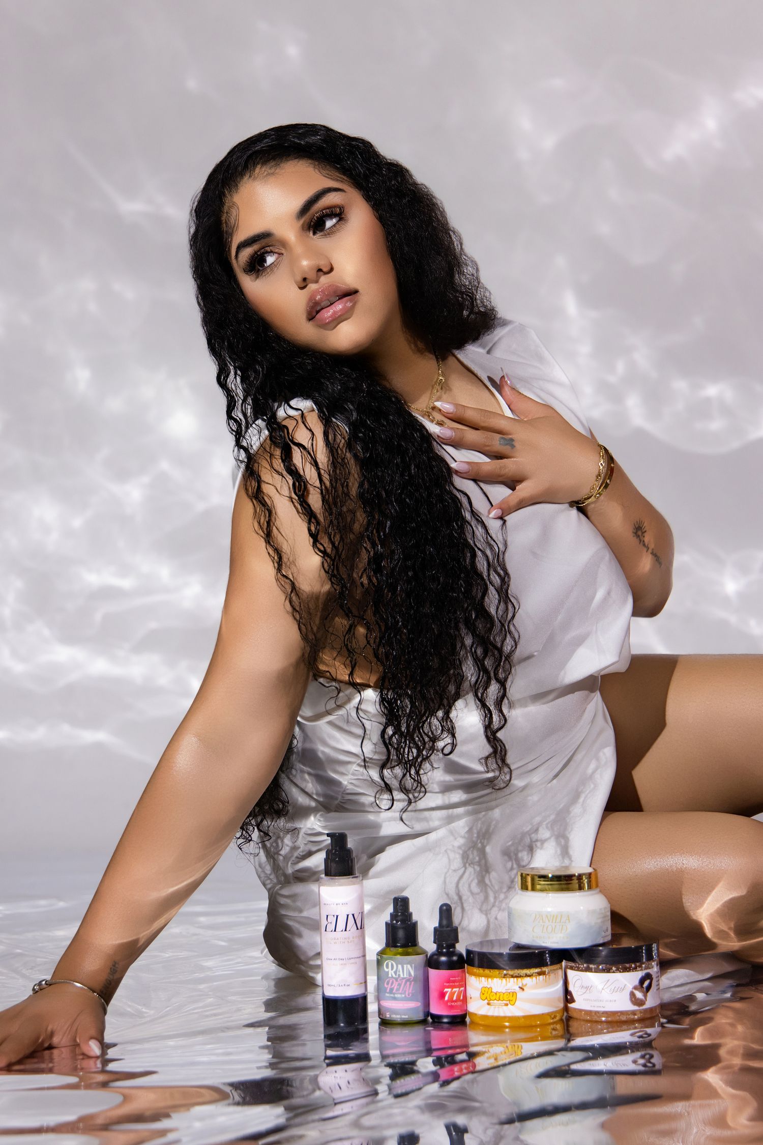 A beauty photoshoot featuring nail polish bottles and cosmetic products arranged on a reflective surface.