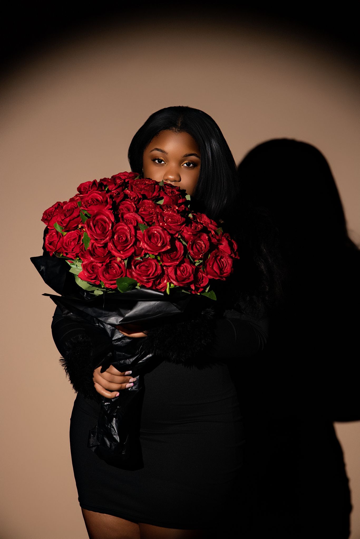 A figure in black holds a dramatic bouquet of red roses against a dark background in an artistic portrait series.