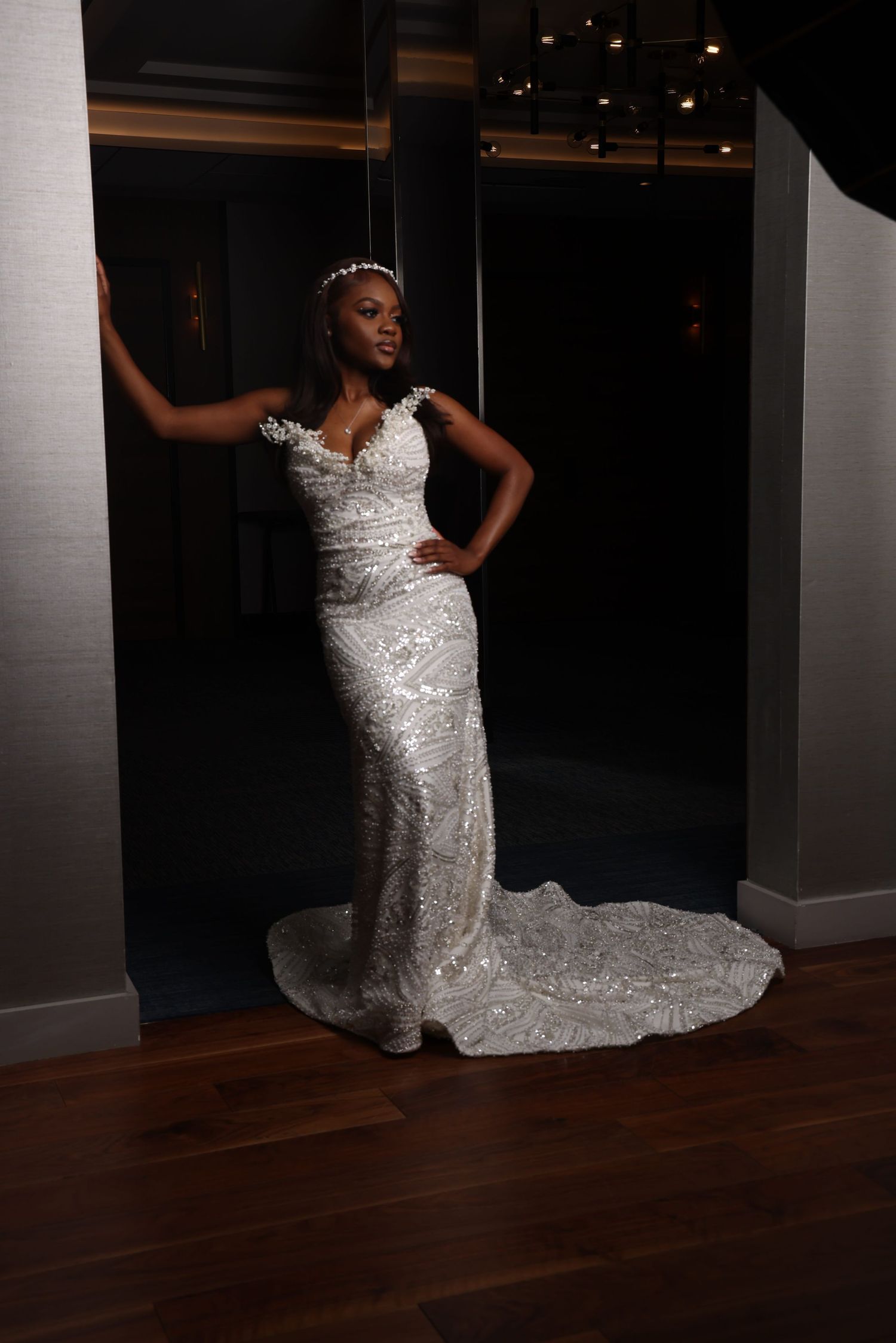 Elegant bridal portrait in sparkling white gown against dark interior.