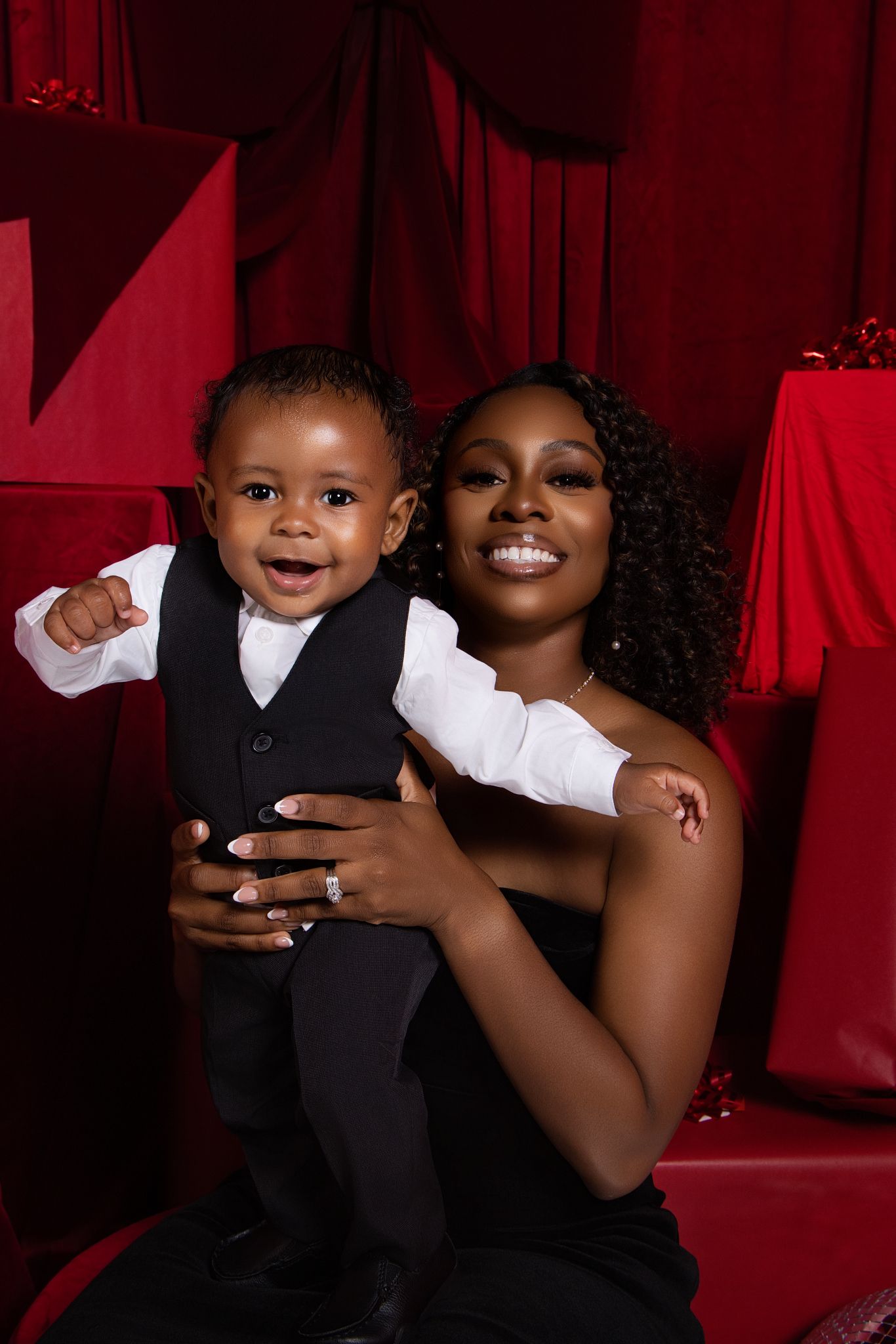 A touching family portrait captured against a dramatic red backdrop with elegant formal attire.