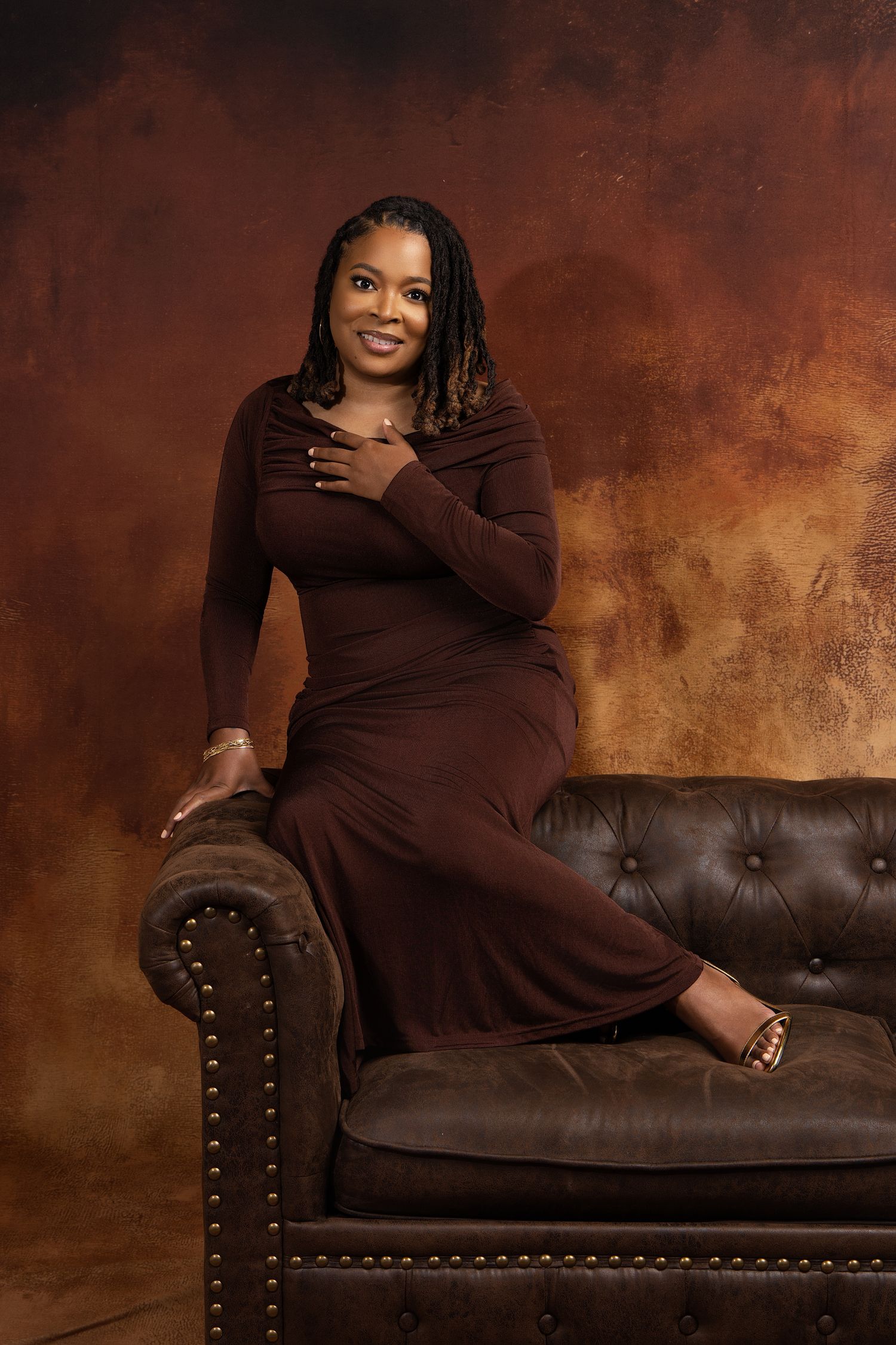 Professional portrait session on a brown leather tufted sofa against a dark rustic backdrop.