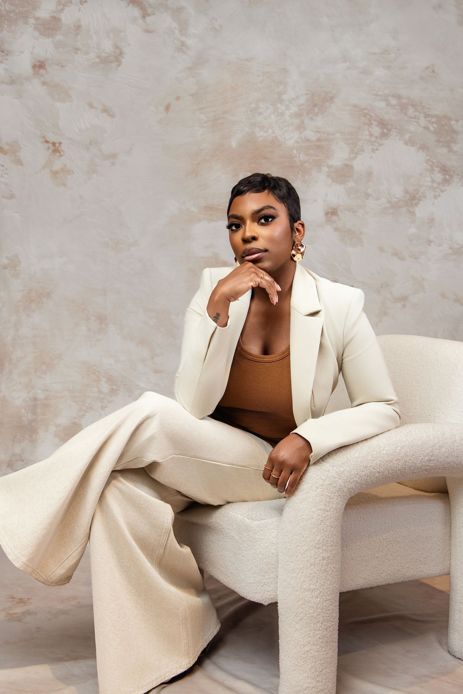 Professional fashion portrait featuring a cream colored pantsuit with brown top against textured beige background.