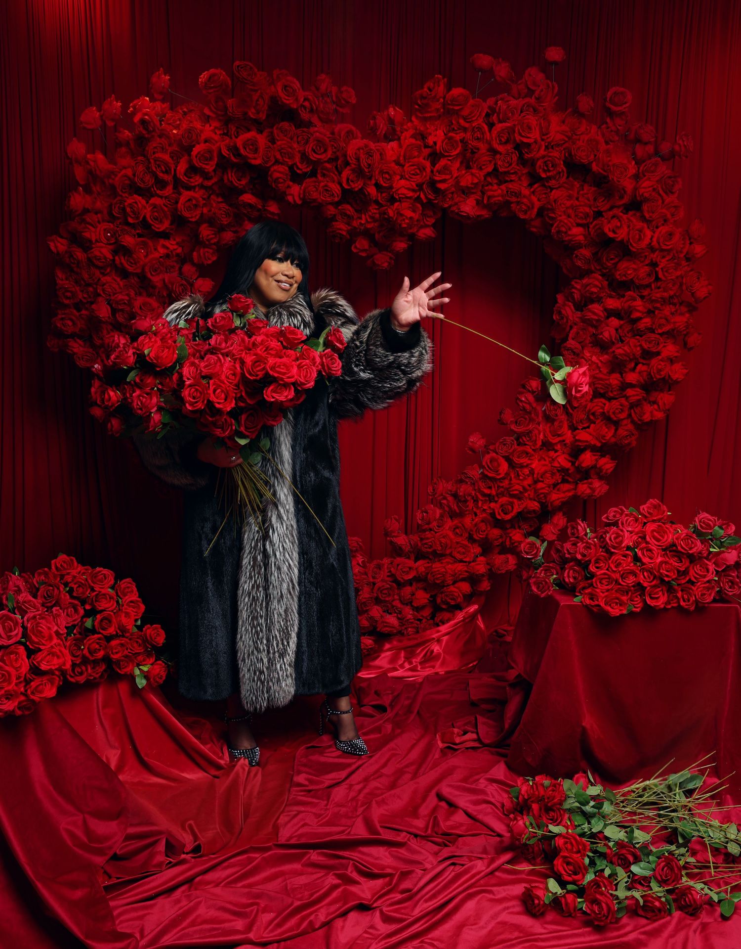 Dramatic fashion photo with model in black fur against red rose wall and flowing fabric.