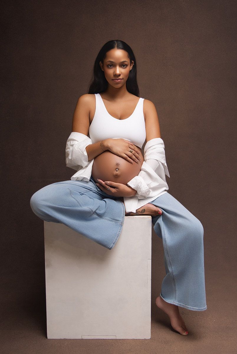 A series of artistic maternity portraits showing a woman in white top and light blue pants seated on a minimalist cube backdrop.