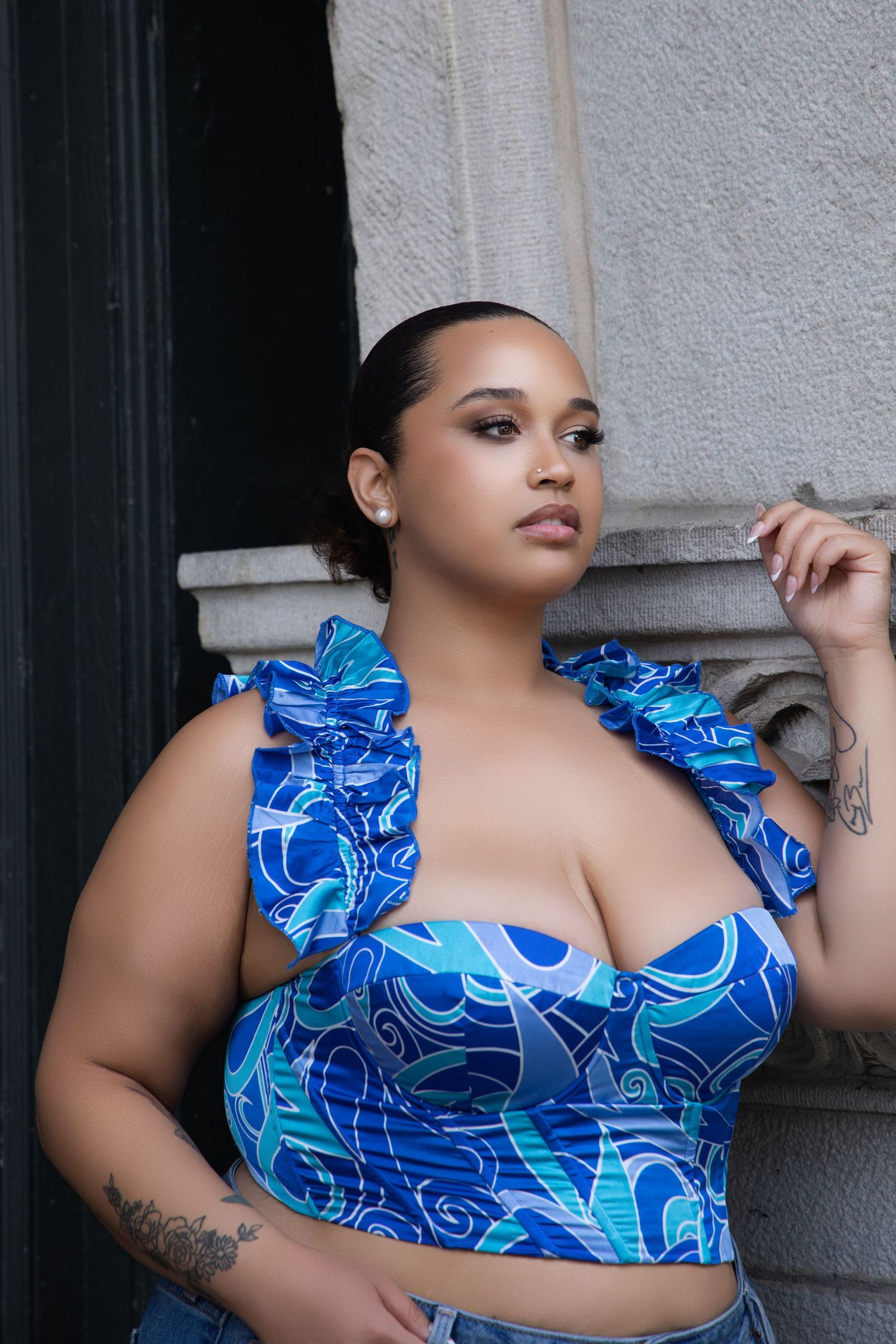 Model wearing blue patterned crop top poses against white wall.