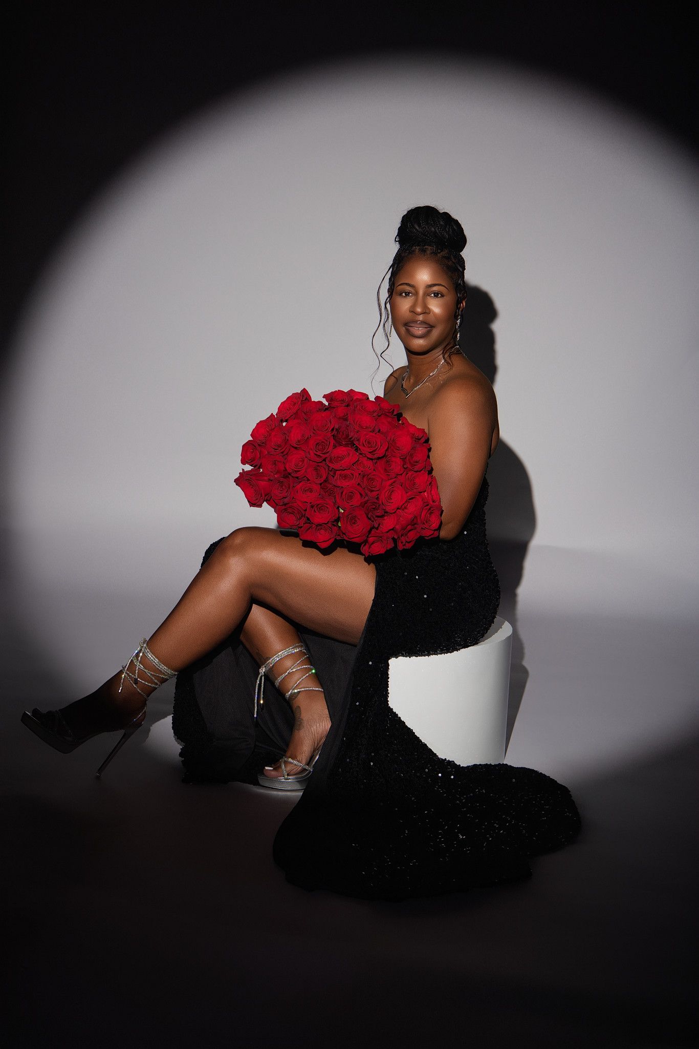 Dramatic black and white boudoir photography with red roses and spotlight creating elegant contrast and shadows.