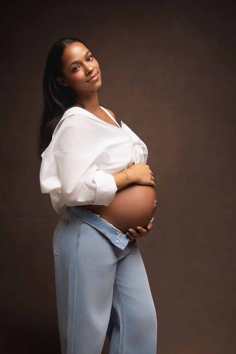 Expectant woman in white blouse and blue jeans poses for three elegant maternity photos against dark background.