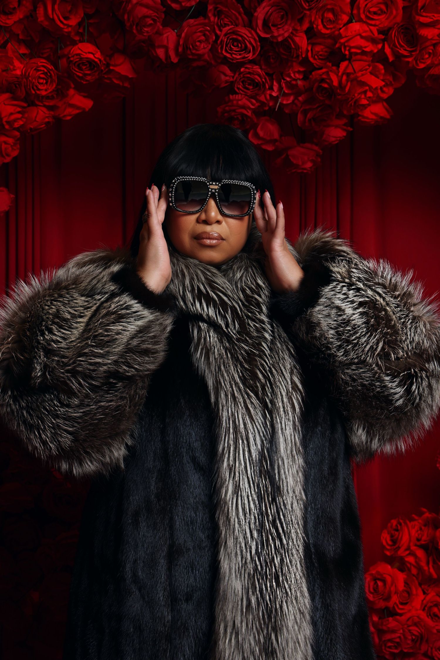 Fashion portrait with fur coat and sunglasses against dramatic red rose background.