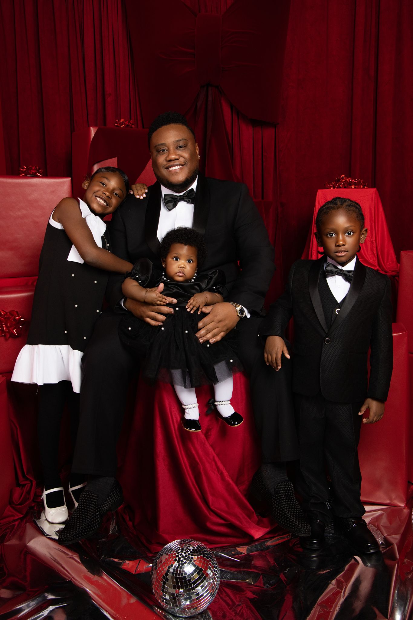 A formal family portrait with adults and children dressed in black and white attire against a luxurious red backdrop.