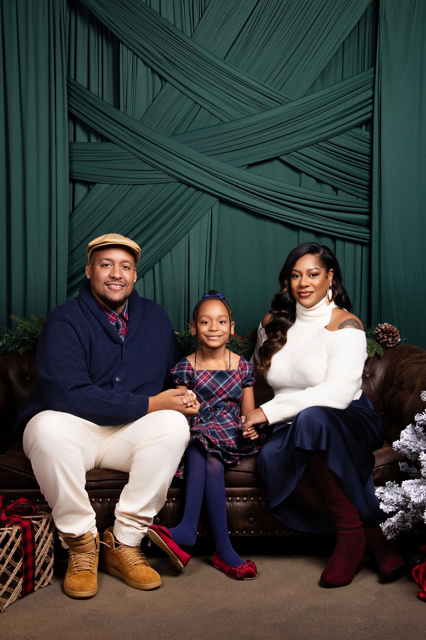 Family members sit together on floor against green textured backdrop in coordinated navy and white outfits.