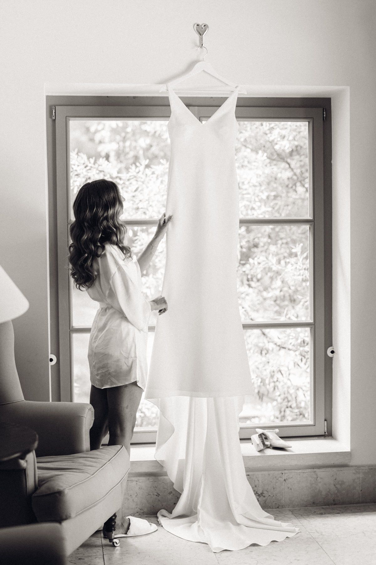 Bride adjusting her dress in front of the window, natural light and timeless elegance