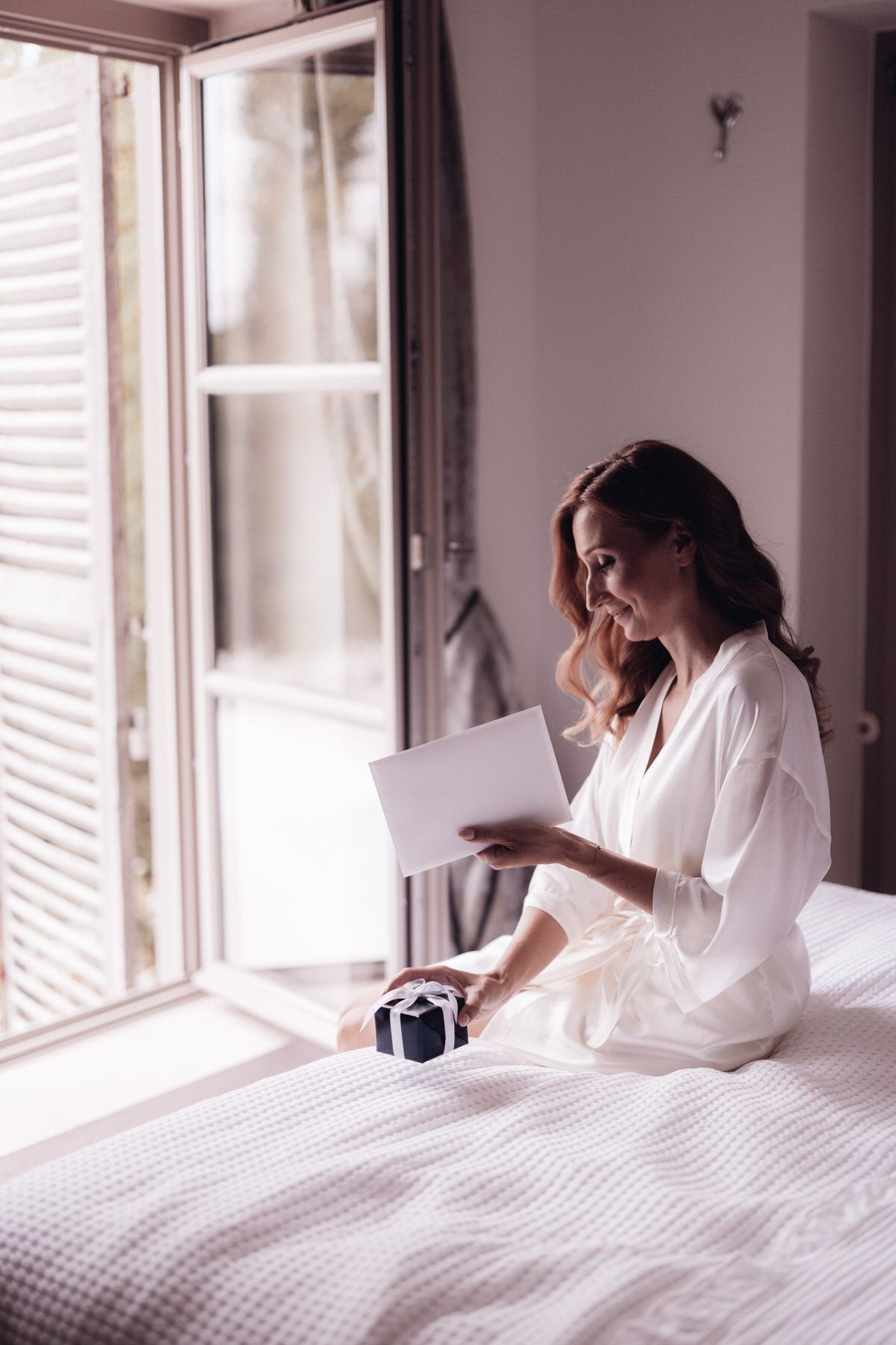 Bride sitting on the bed by the window, calm and emotional getting ready moment