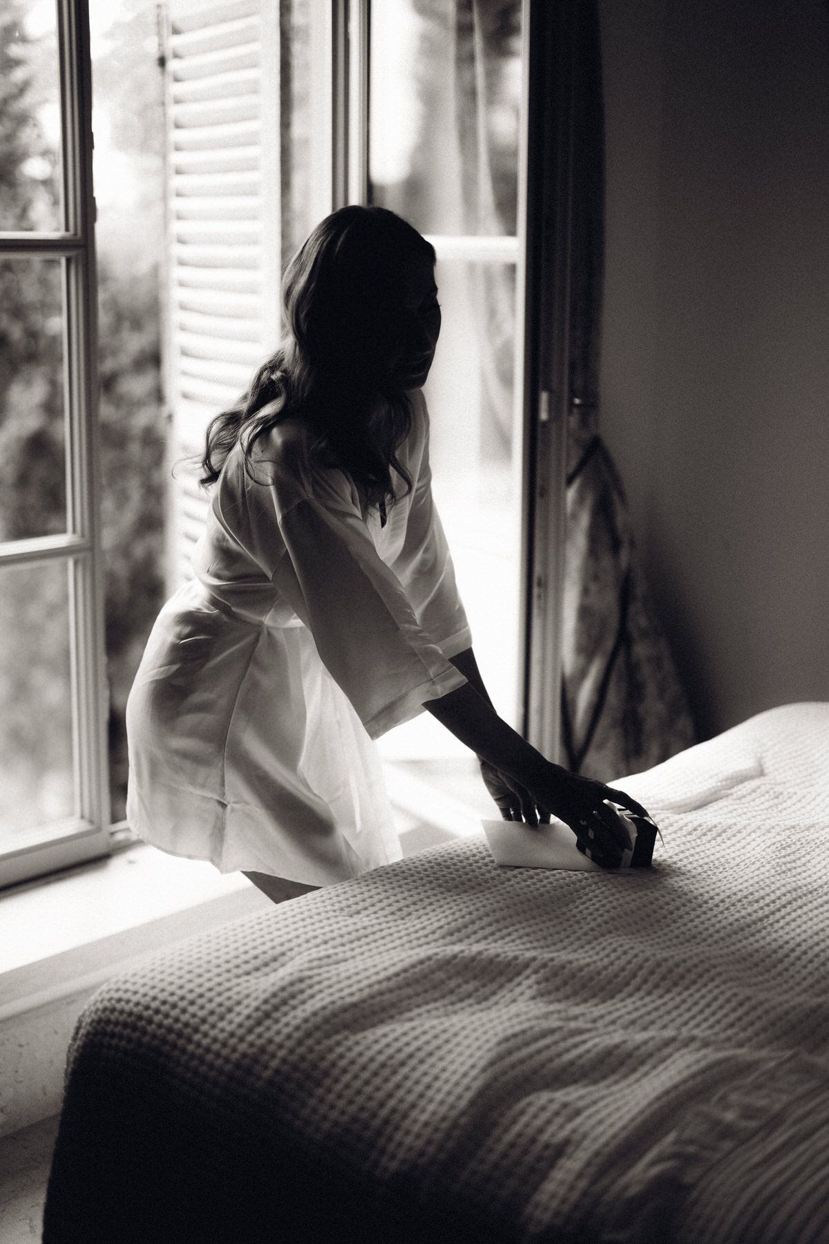 Bride sitting on the bed by the window, calm and emotional getting ready moment