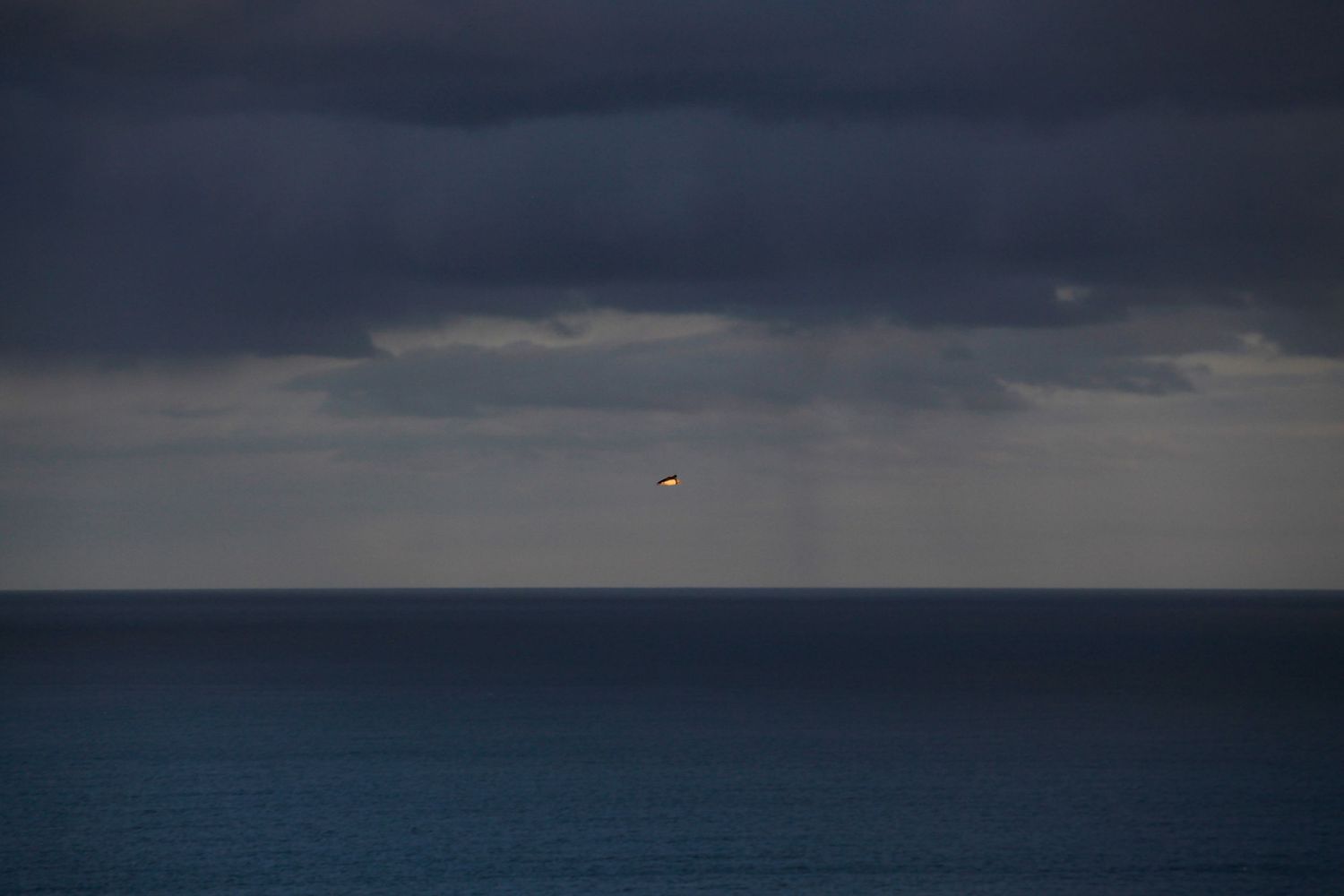Dark moody seascape with stormy clouds and a bright spot on the horizon.