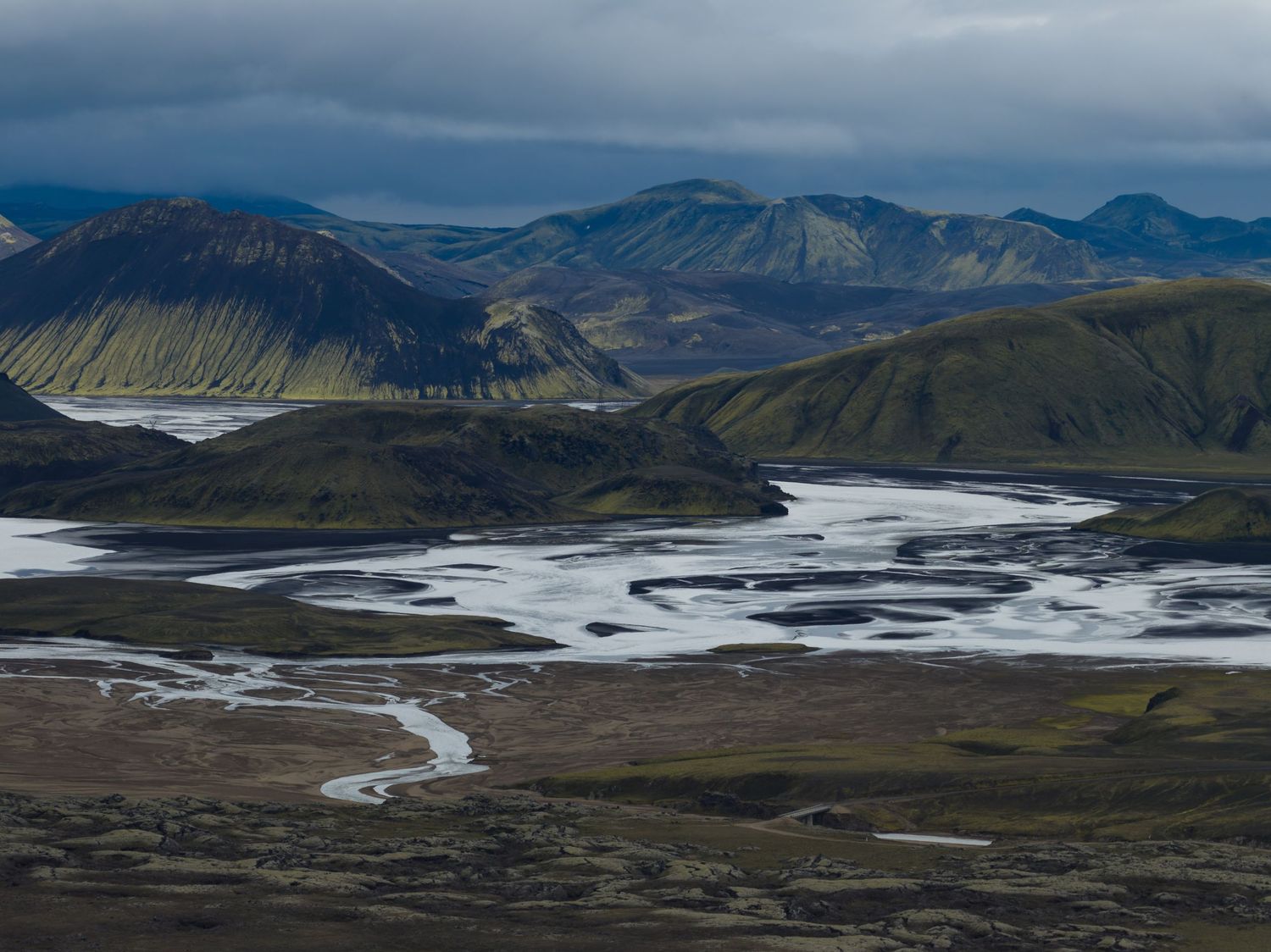 Sweeping vista of braided rivers flowing through snow-patched mountain valleys.