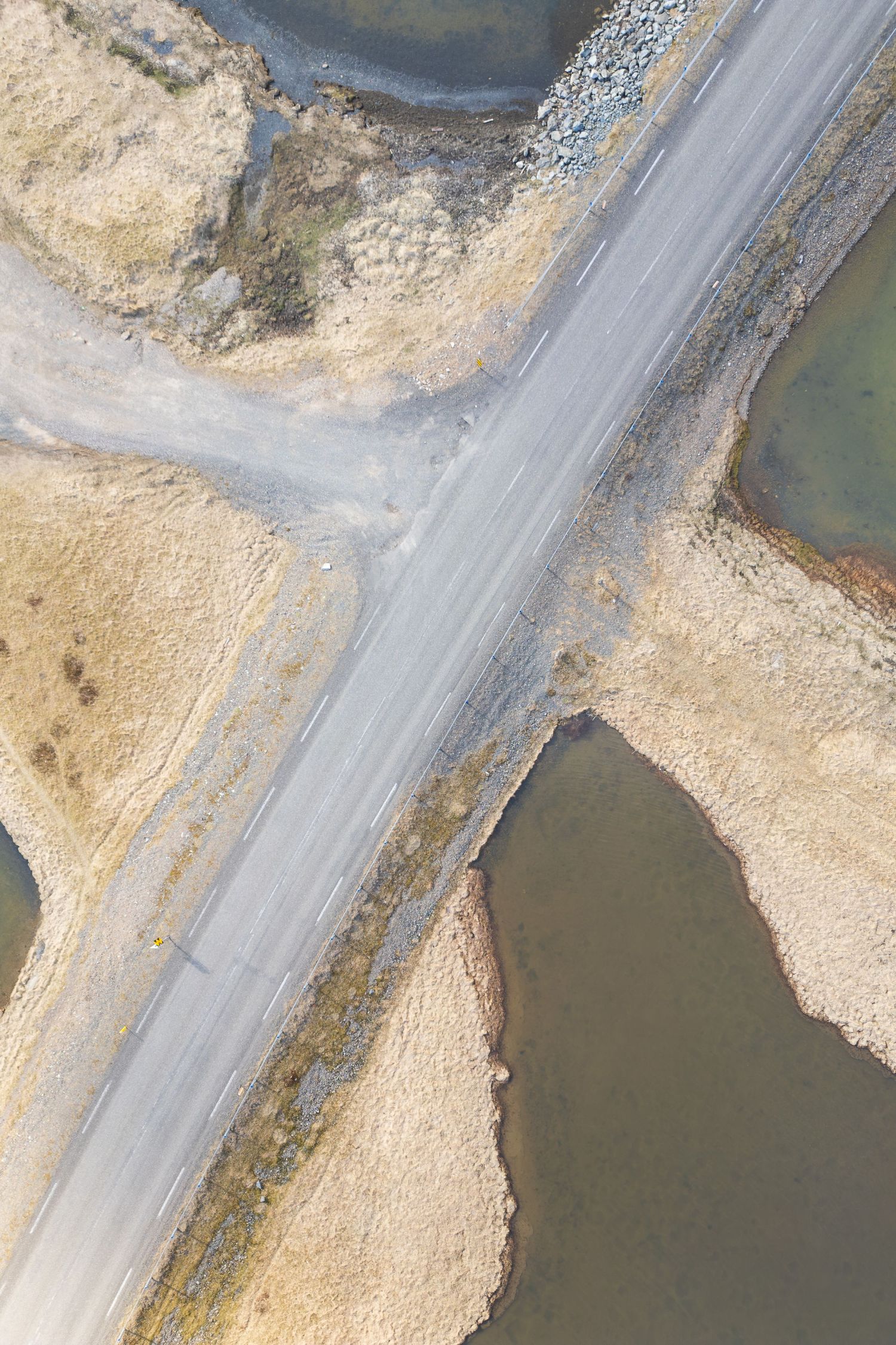 Aerial view of a winding road along a sandy coastline with water on one side.