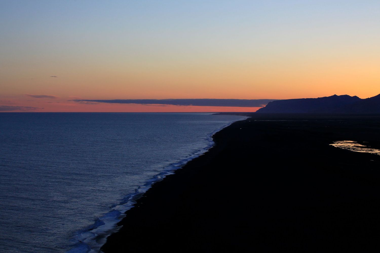 Silhouette of coastal cliffs at sunset with orange and purple sky.