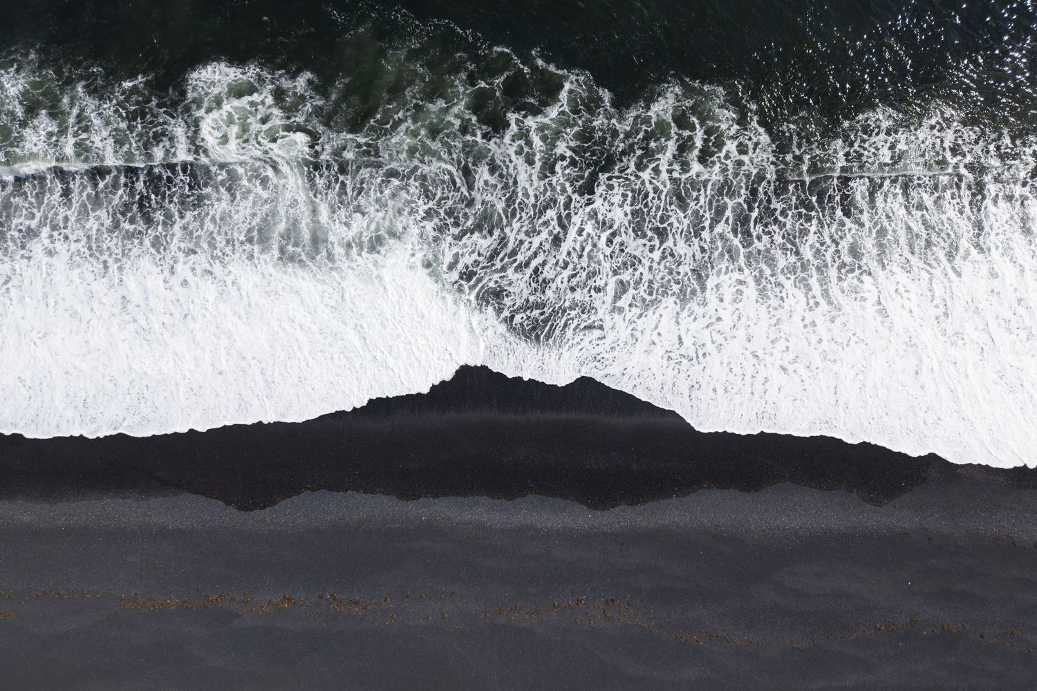 Dramatic aerial view of ocean waves crashing on black sand beach.