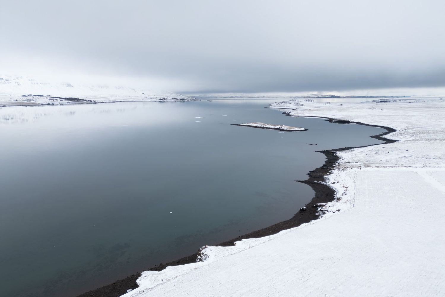 Snowy shoreline meeting dark water under an overcast sky in winter.