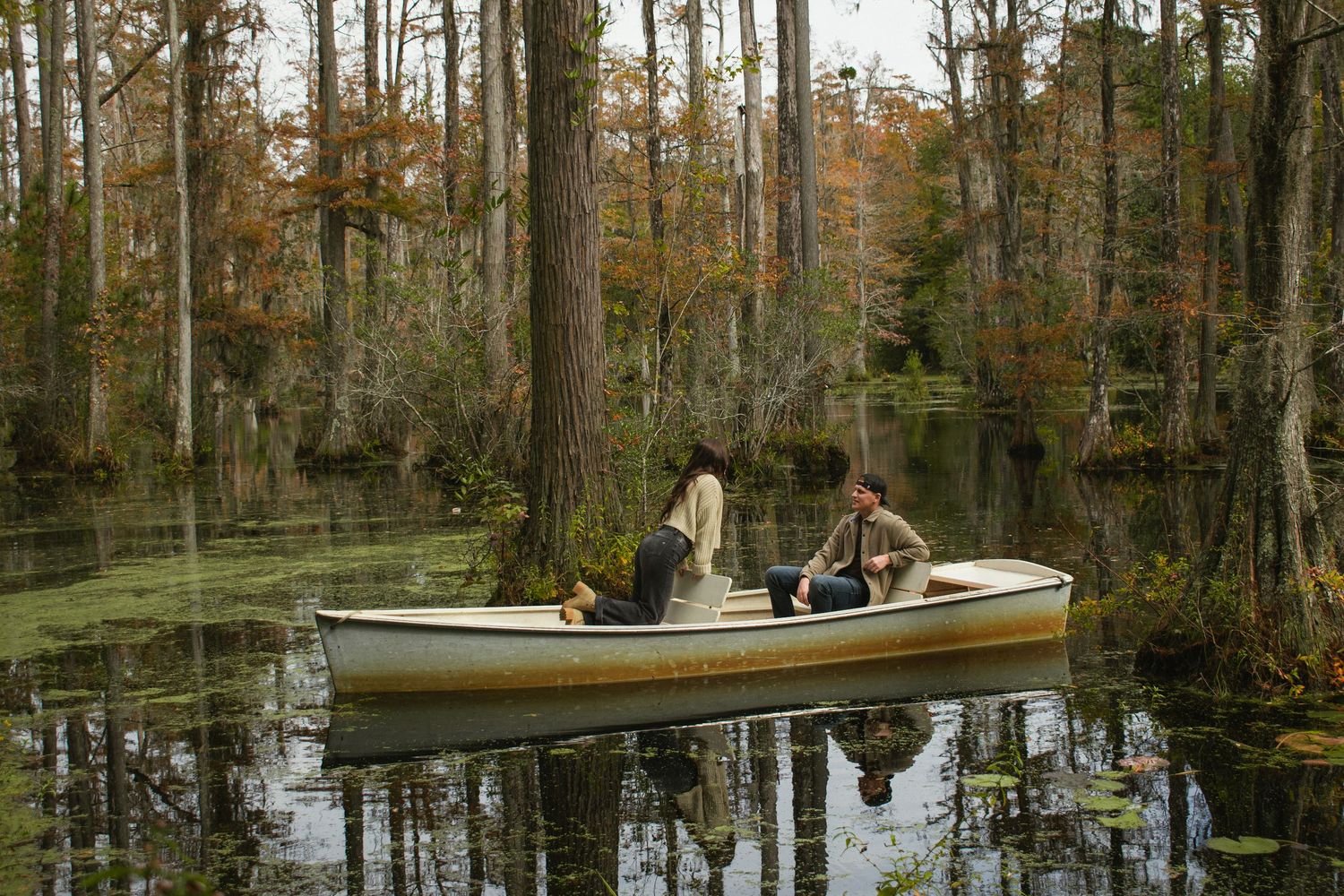 Boats floating on calm swamp waters surrounded by cypress trees in autumn.