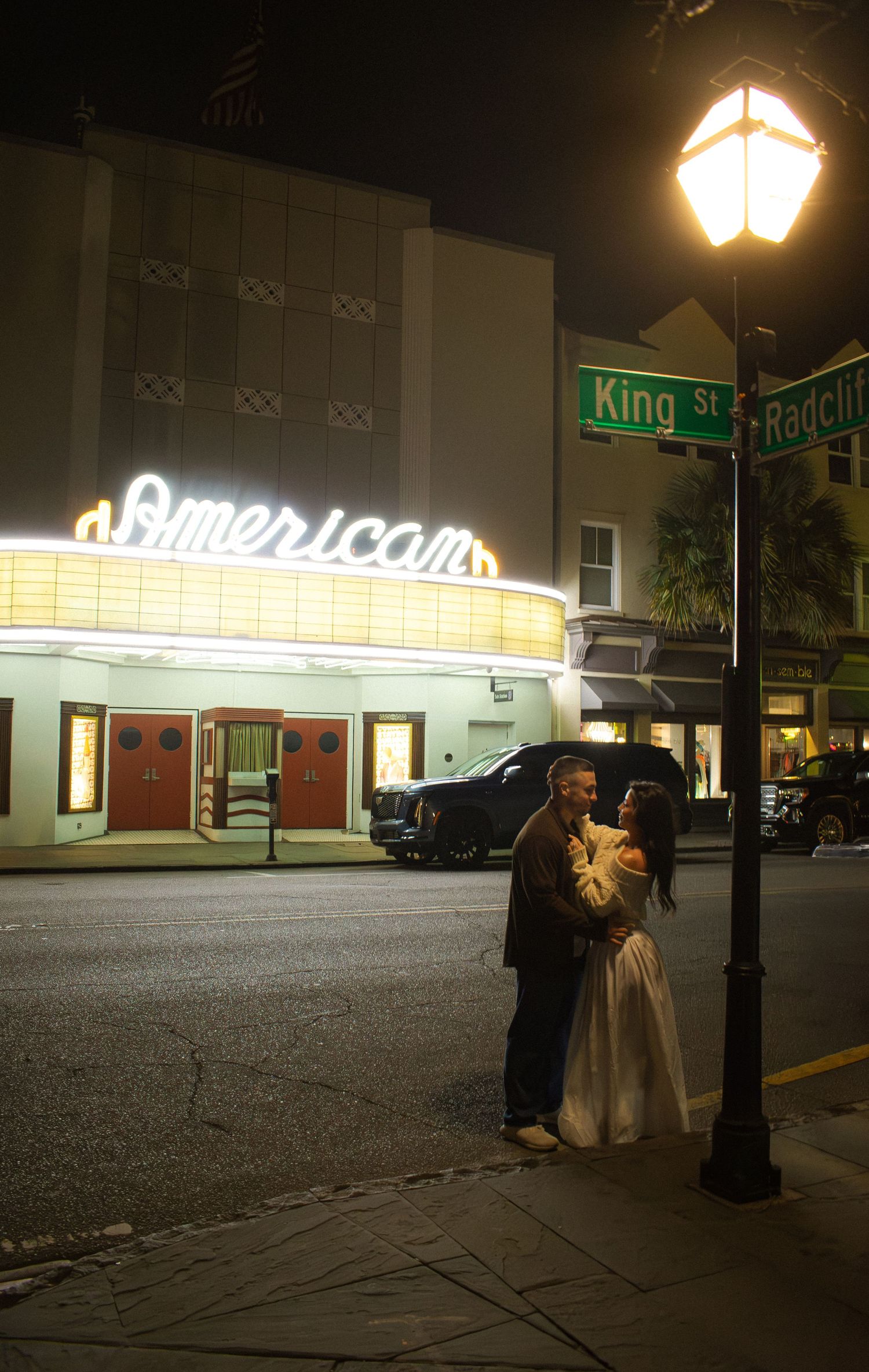 Nighttime street scene with illuminated American sign and street lamps.