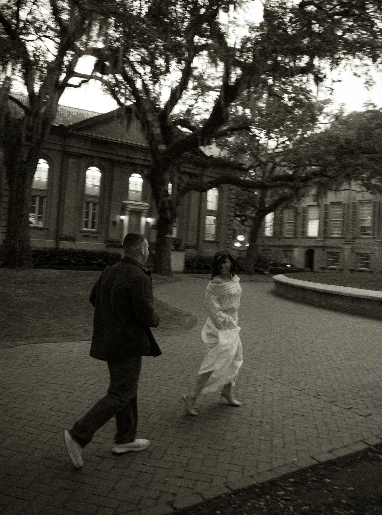 People walking on brick pathway outside historic buildings at dusk.