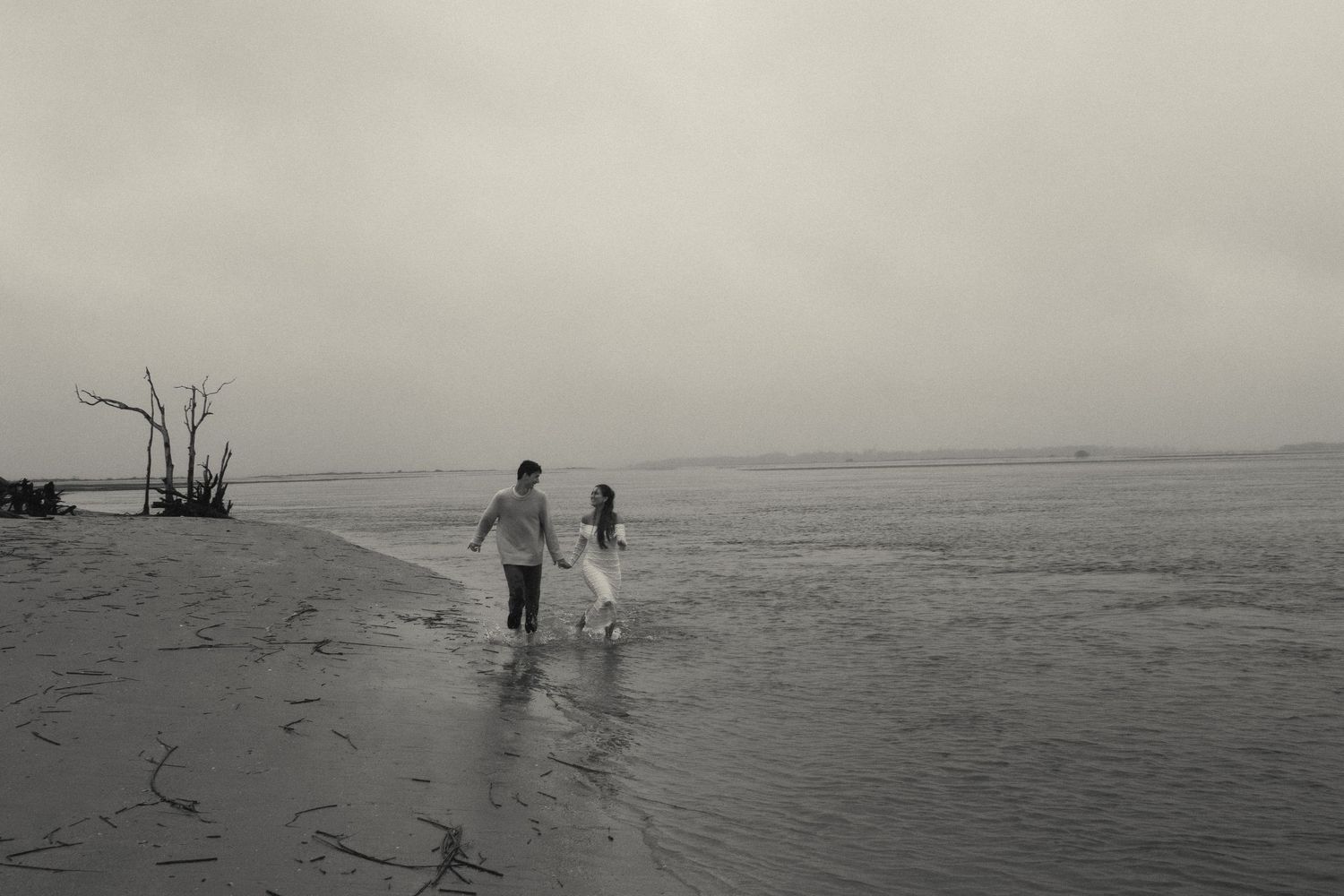 A couple walking together on a misty beach in black and white.