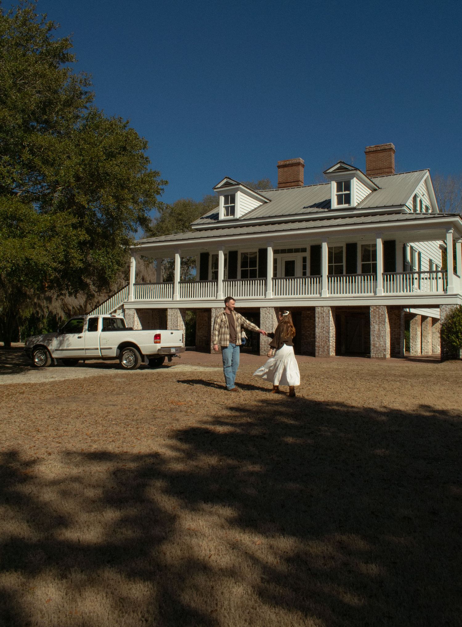 White colonial style house with wraparound porch and multiple columns in bright sunlight.