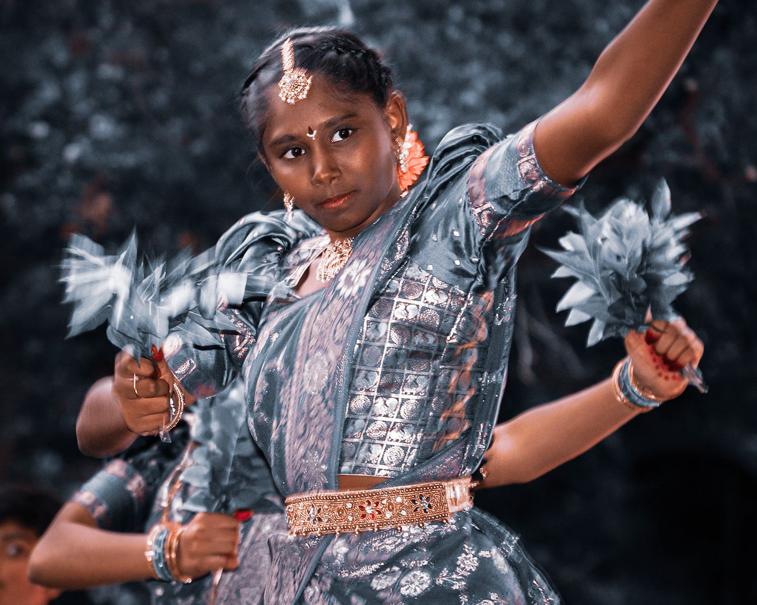 Performer in silver sequined costume strikes dynamic dance pose against dark background.