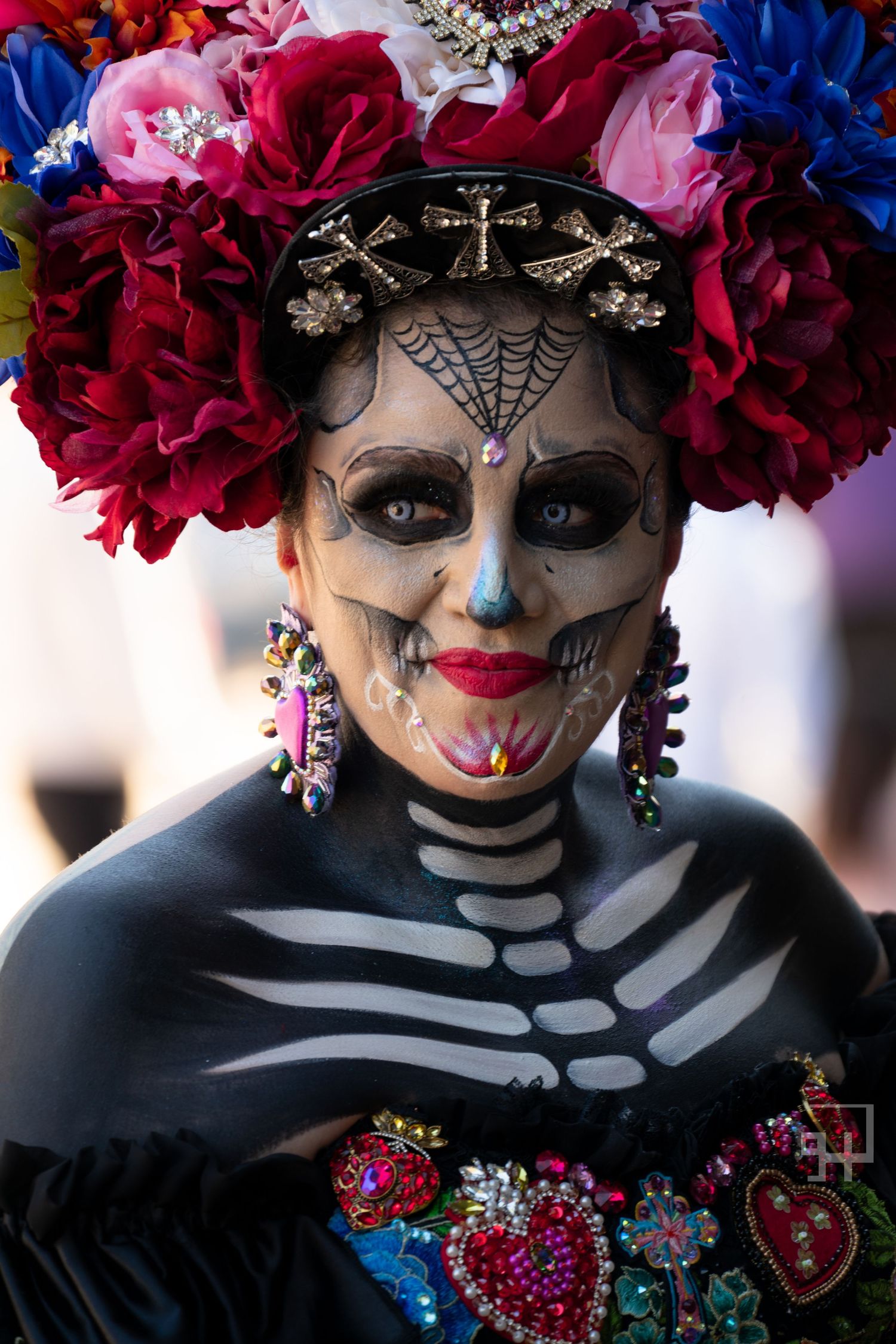 Artistic Day of the Dead makeup and costume featuring pink floral crown, black skeleton face paint, and colorful jewelry. By grain n glass