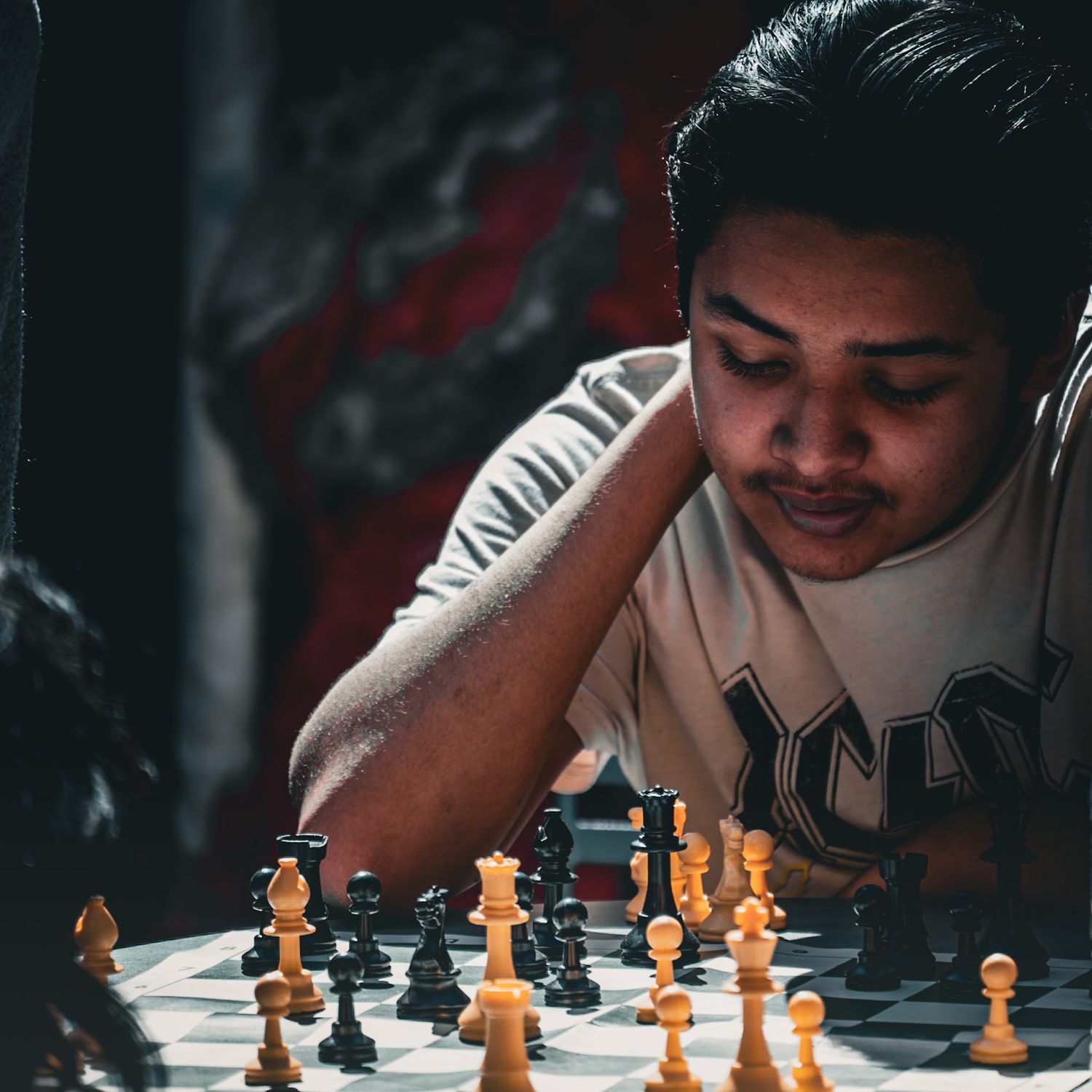 Person concentrating while playing chess with wooden pieces on a board in dramatic lighting. Shot by a Seguin photographer at grain n glass