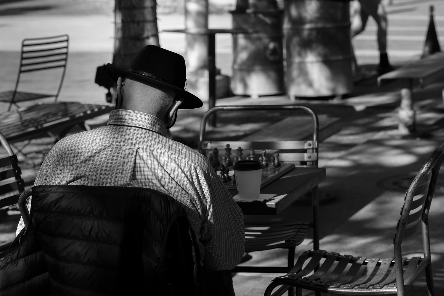 Elder man in a hat sitting at a chess table alone. A black and white photo Captured by a Seguin photographer at grain n glass