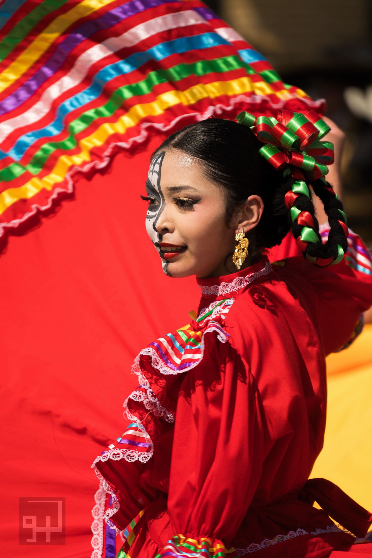 Traditional Mexican dancer in bright red dress performs energetic dance movements against colorful backdrop.