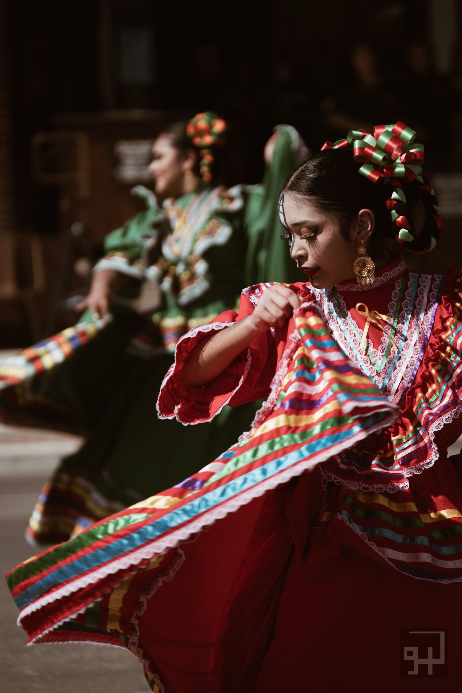 Traditional Mexican dancer in vibrant red dress with colorful ruffles performs a spinning movement during cultural dance.