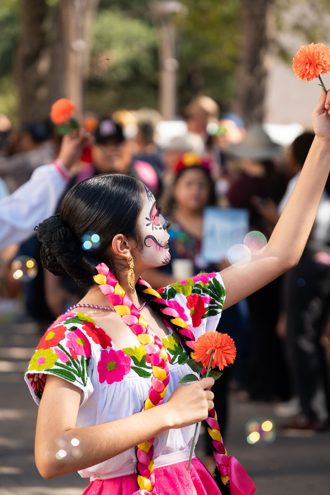 Performer in traditional dress with floral accessories dances during cultural celebration.