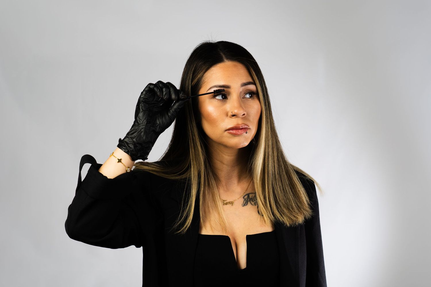Model in black blazer and gloves poses confidently against white backdrop.