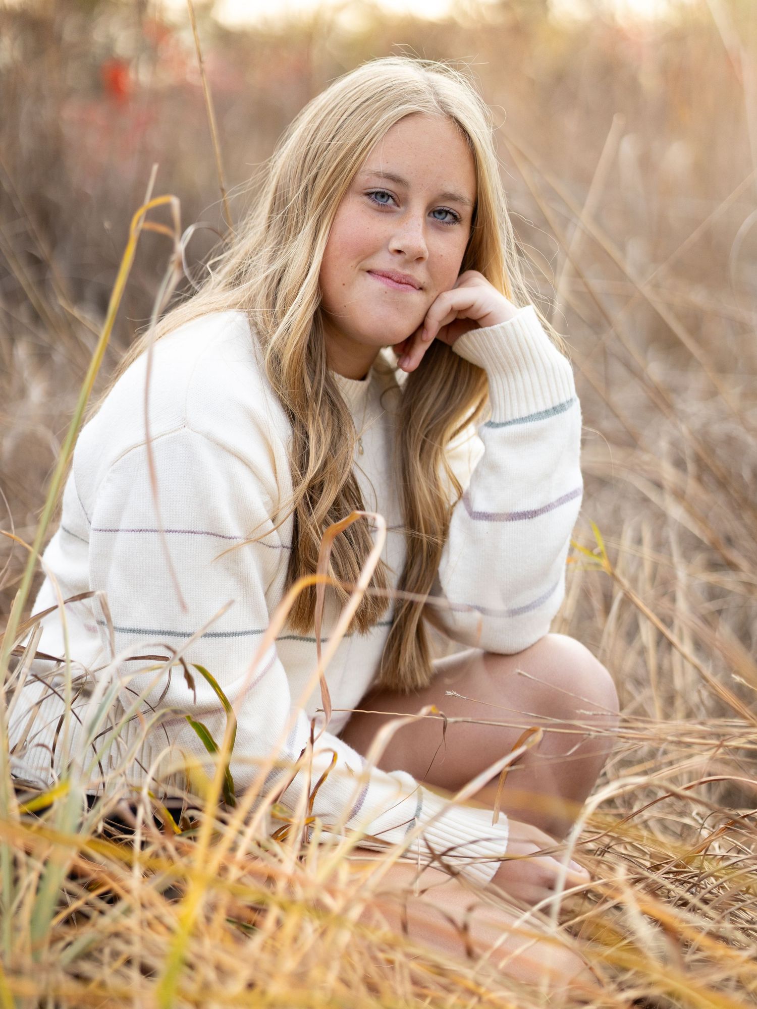 senior girl portrait crouching in tall grass with fall colors