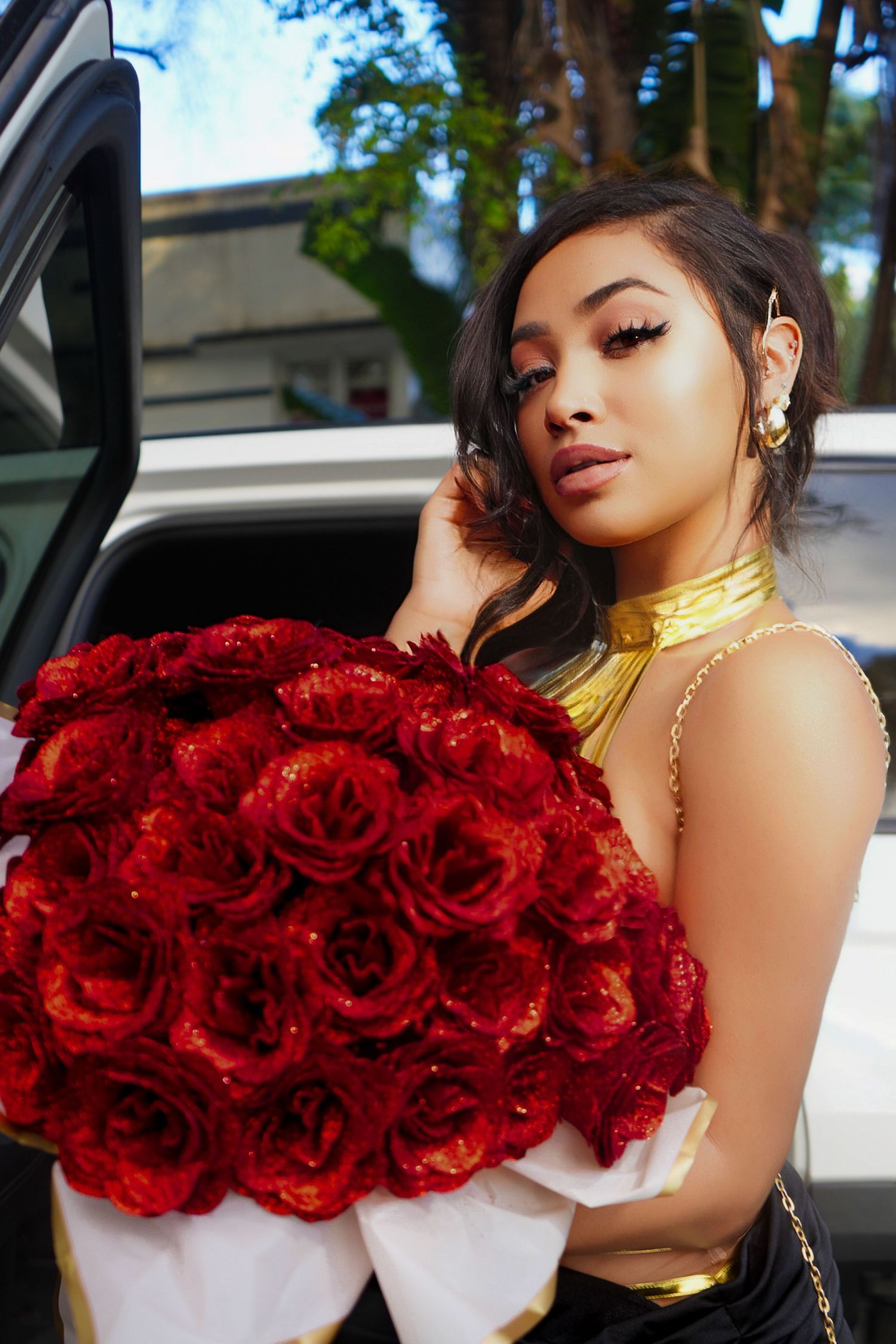 A person in a car holding a large bouquet of deep red roses against a white interior.
