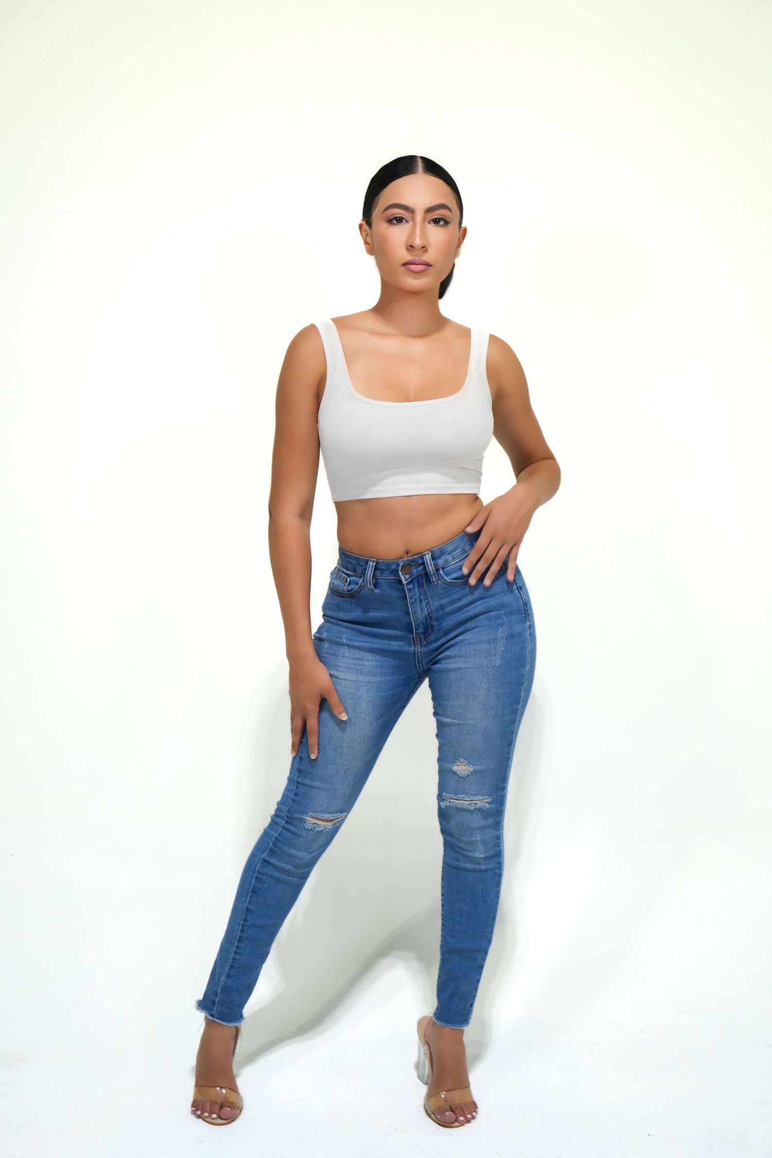 Model wearing distressed blue jeans and white crop top poses against white background in three different stances.