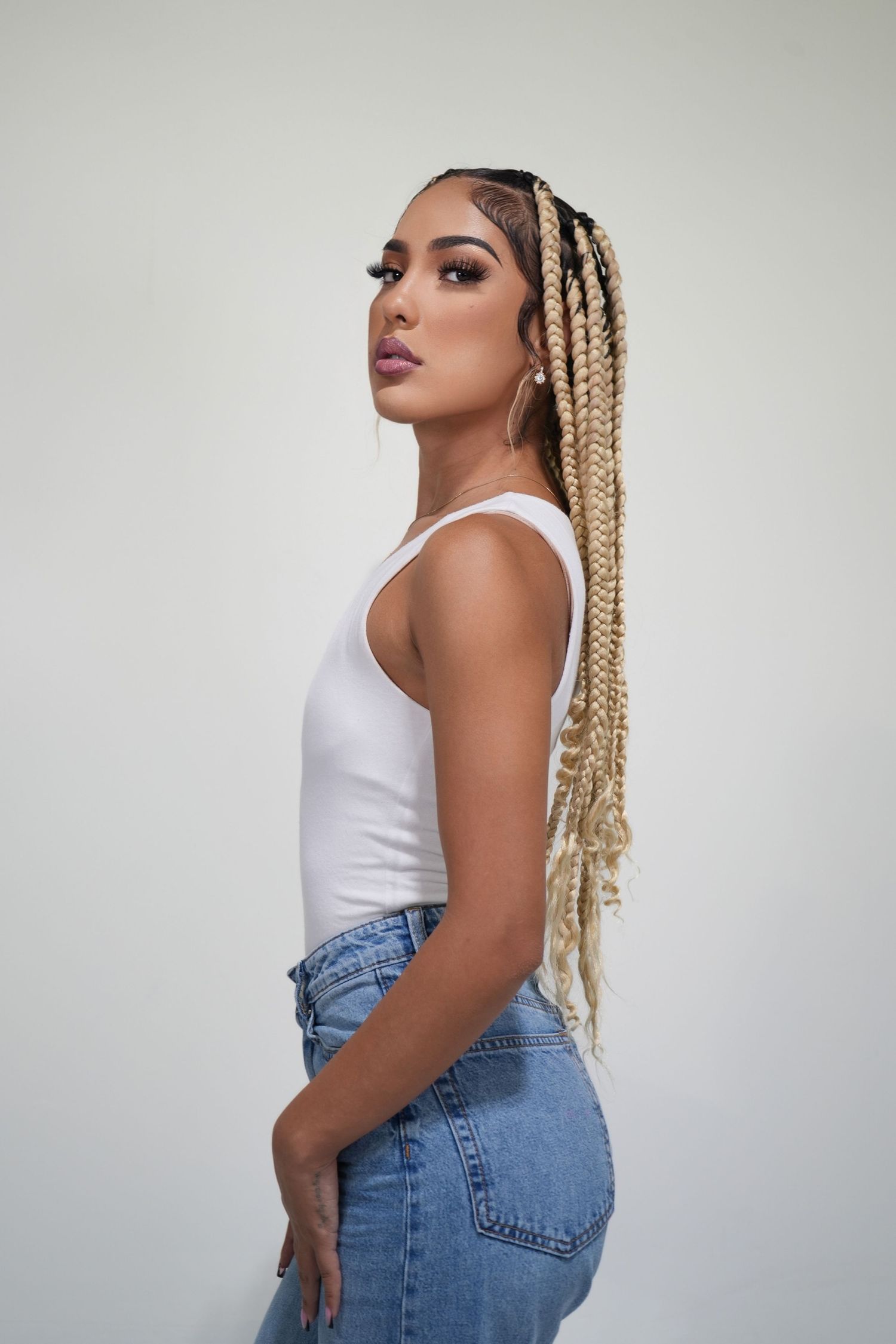 Side profile of model in white tank top and jeans with long blonde braided hair.